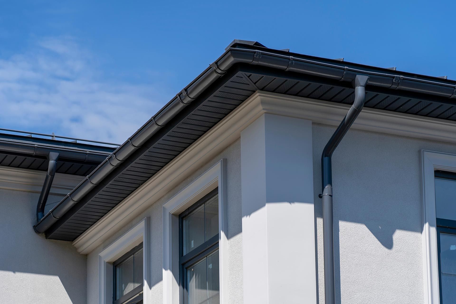 Close-up of a white house exterior with dark roof eaves and blue sky above Close-up of a white house exterior with dark roof eaves and blue sky above
