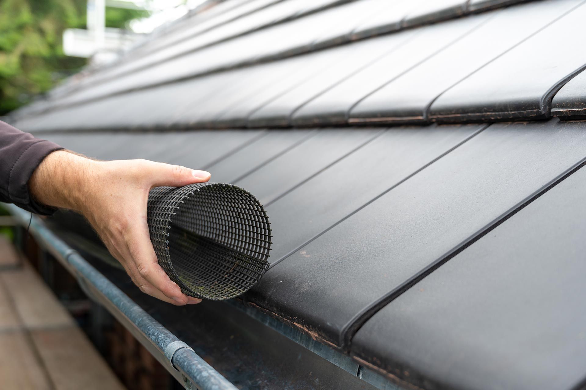 Hand placing a rolled black mesh gutter guard on a roof gutter
