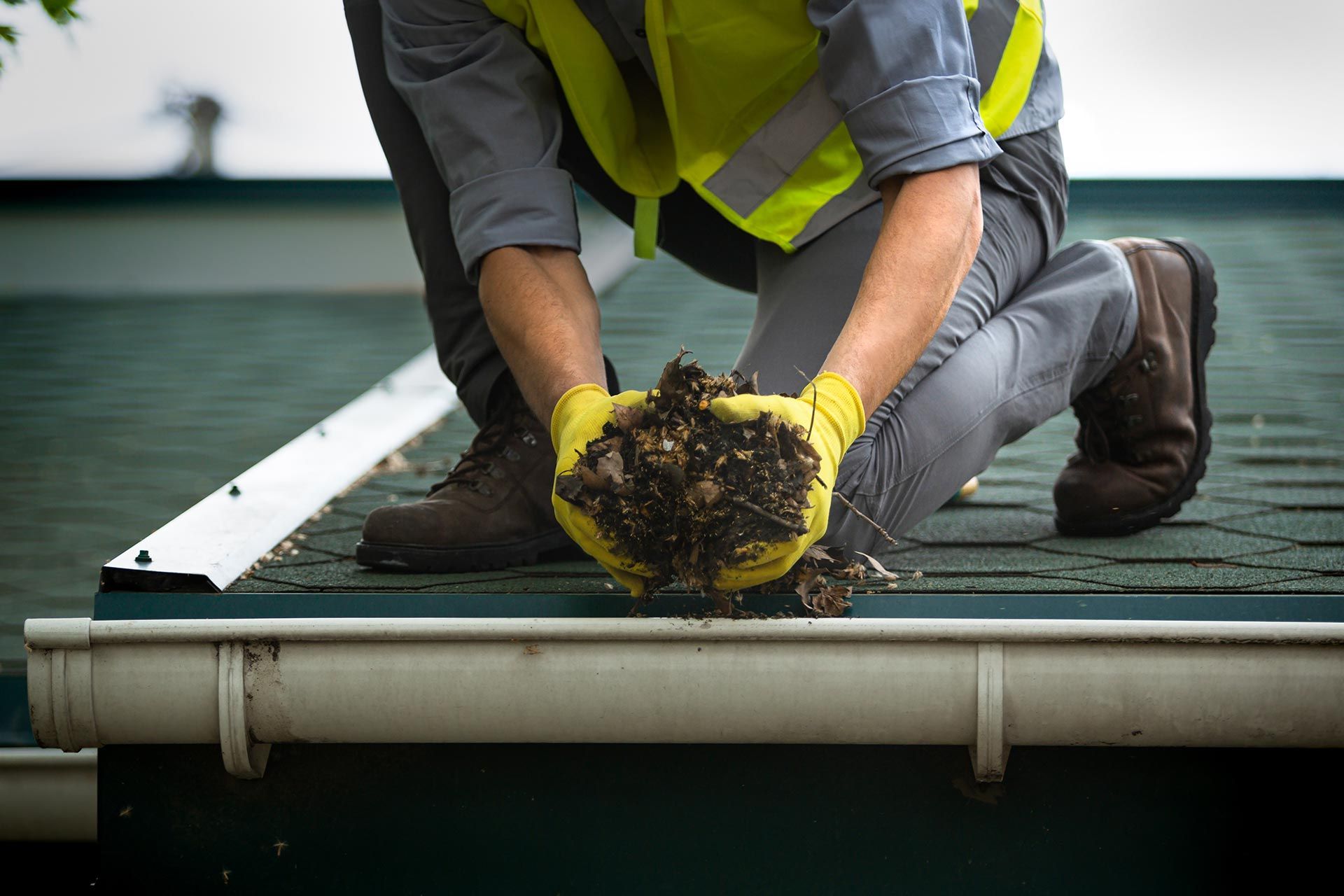 Worker in yellow vest cleaning debris from a rooftop gutter Worker in yellow vest cleaning debris from a rooftop gutter