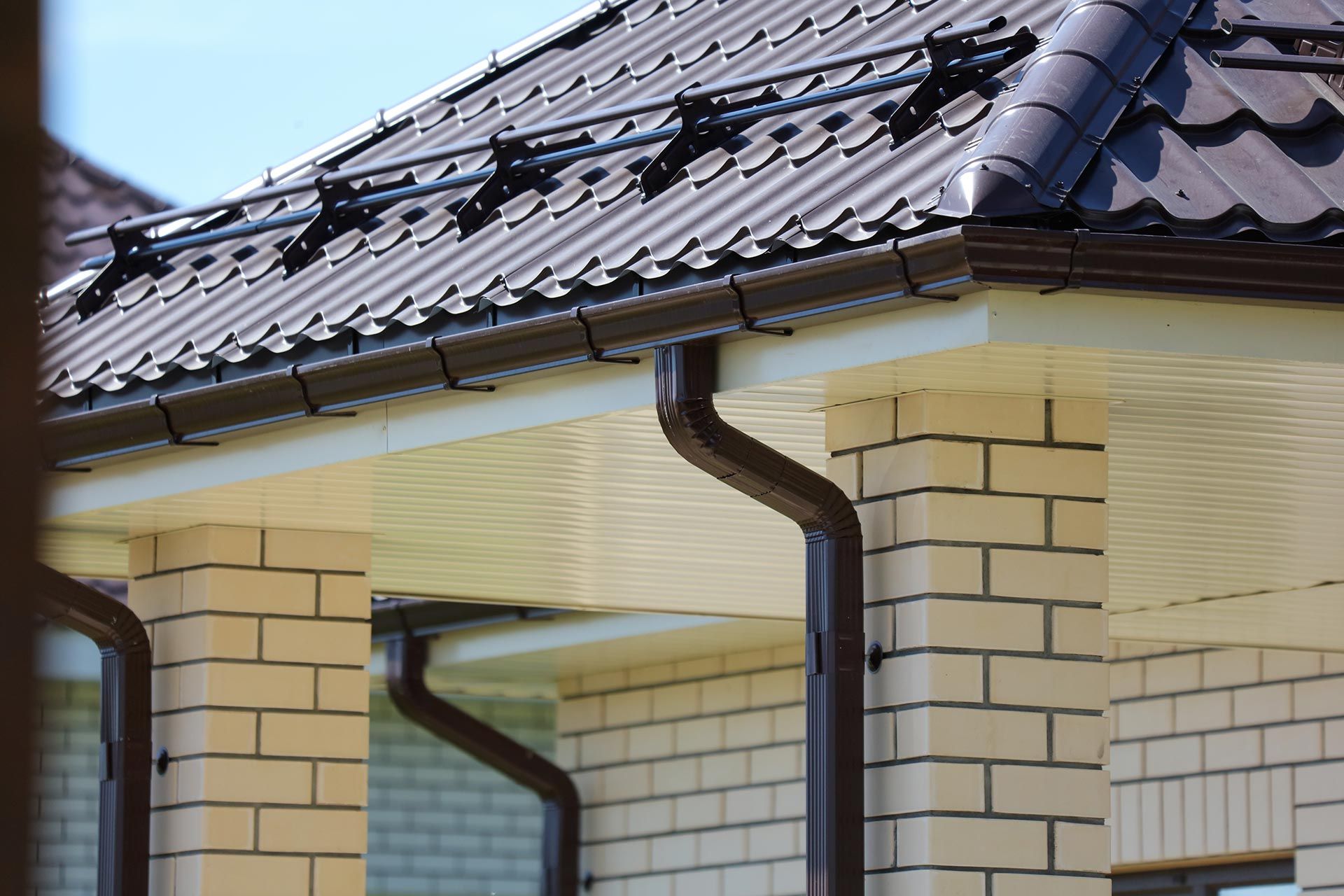 Brick house exterior with dark tiled roof and two beige columns under a covered porch Brick house exterior with dark tiled roof and two beige columns under a covered porch