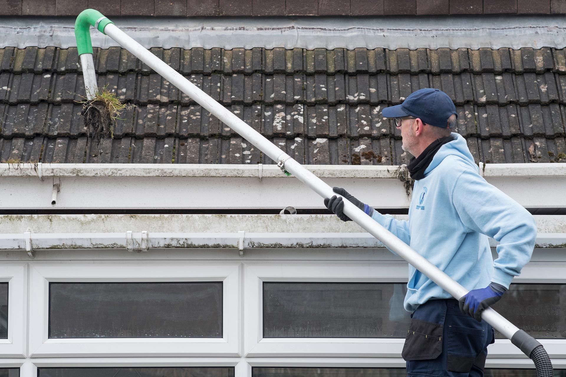 Worker cleaning roof gutter with a long pole beside a house Worker cleaning roof gutter with a long pole beside a house