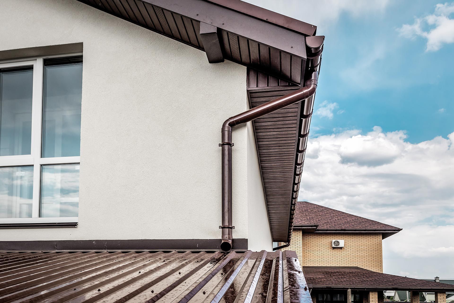 Exterior corner of a house with white wall, brown roof, and blue sky Exterior corner of a house with white wall, brown roof, and blue sky