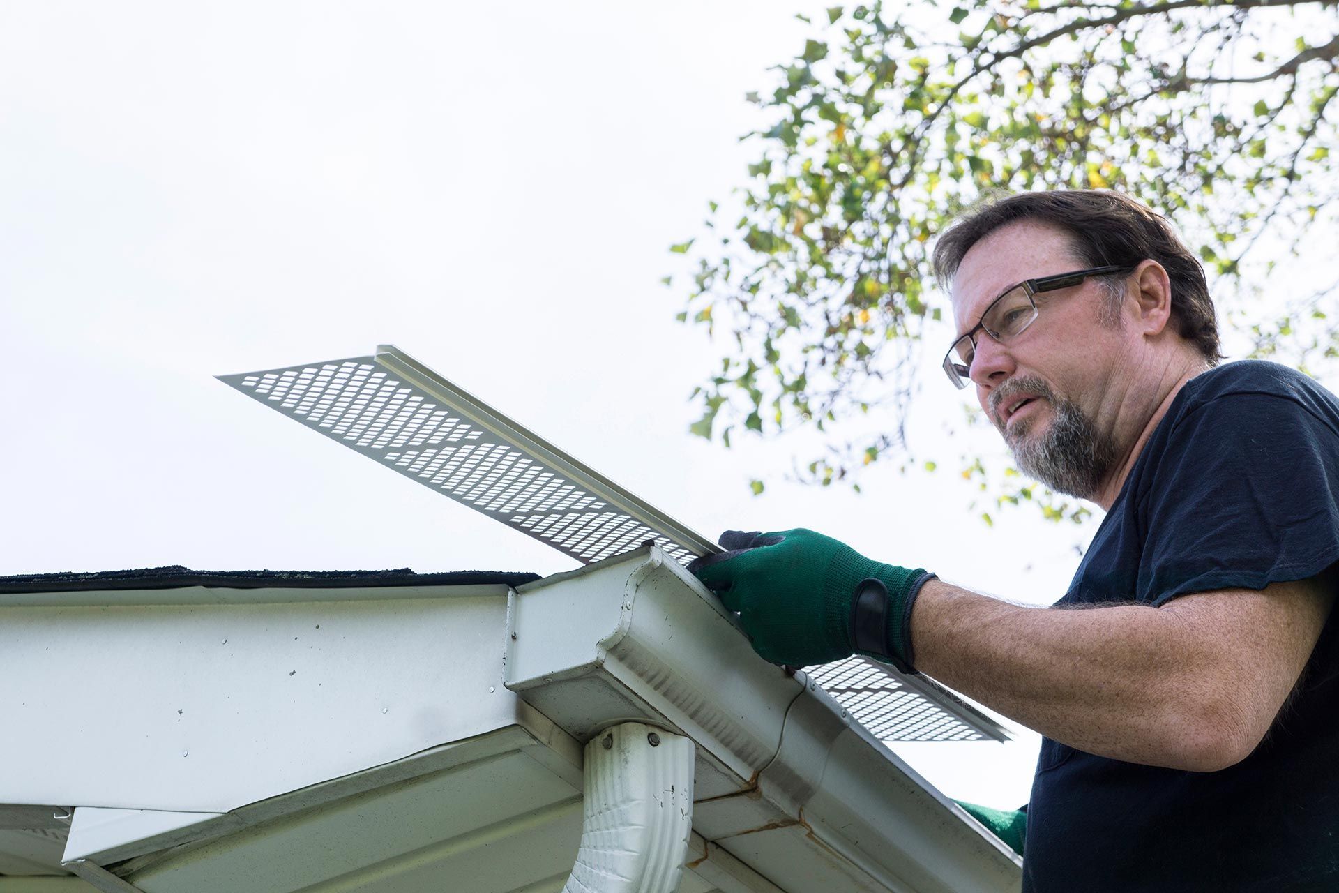 Man installing a metal gutter guard on a house roofline outdoors