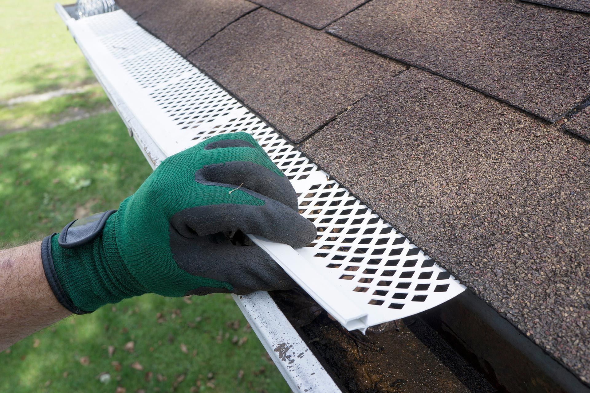 Gloved hand installing a white perforated gutter guard on a house roof edge