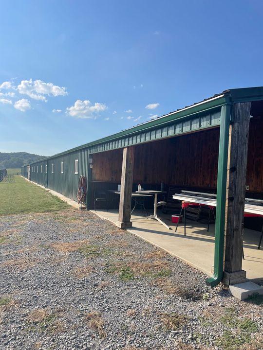 Long covered outdoor storage bay with green roof, gravel foreground, and red equipment inside under blue sky Long covered outdoor storage bay with green roof, gravel foreground, and red equipment inside under blue sky