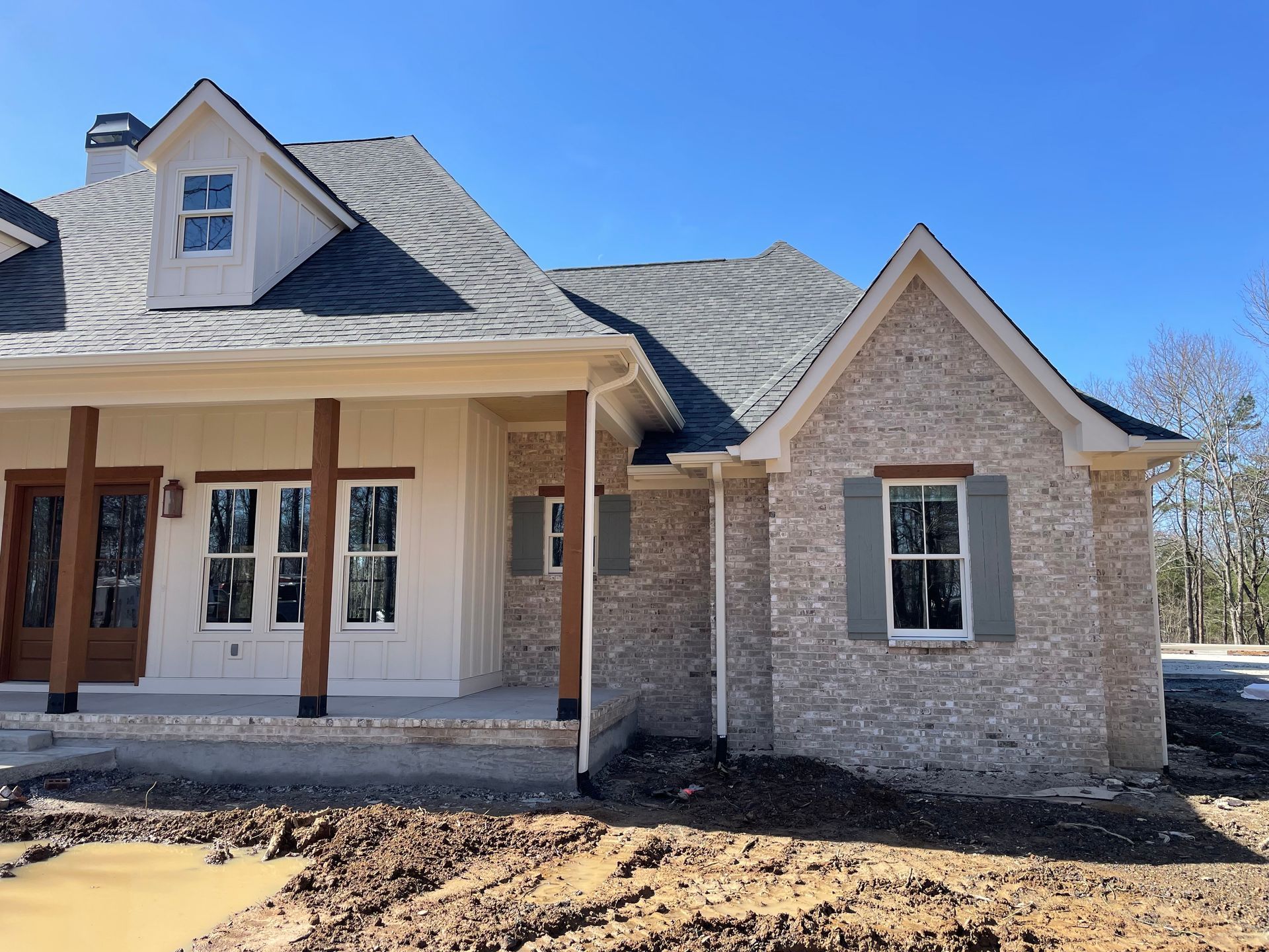 Front exterior of a newly built house with stone siding, gray roof, and covered porch under a blue sky