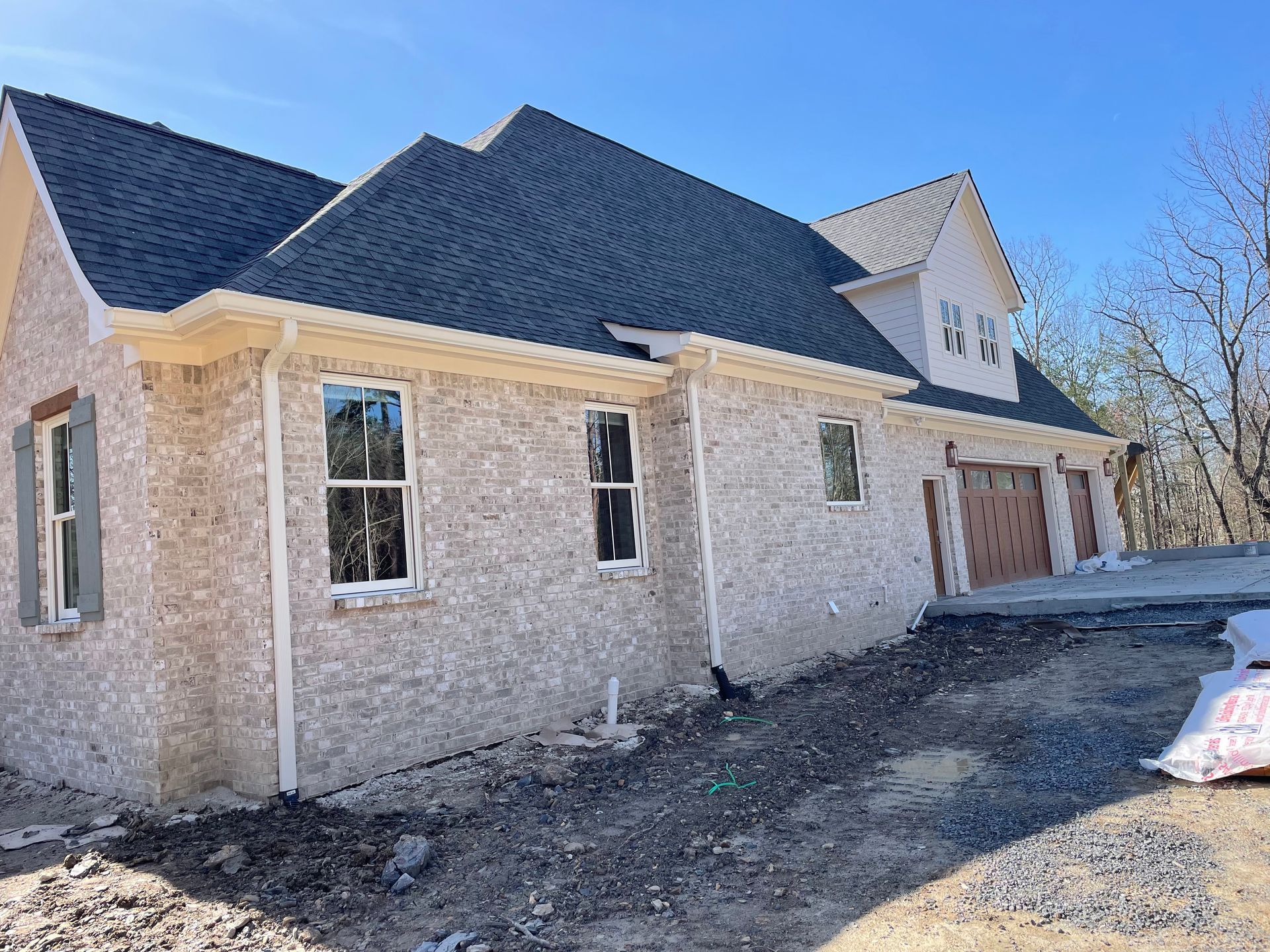 New brick house with dark roof and garage under construction on a dirt driveway