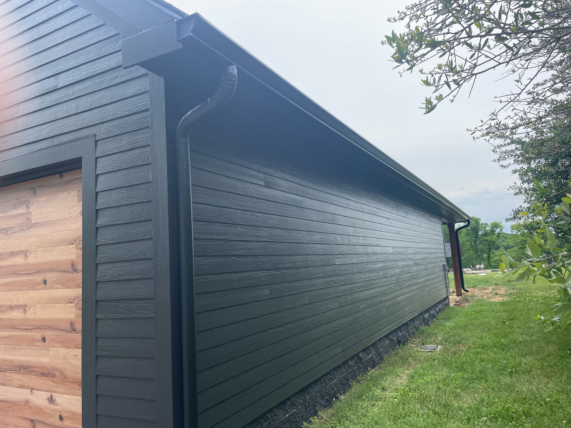 Black-painted wooden shed with a sloped roof beside a grassy yard and trees