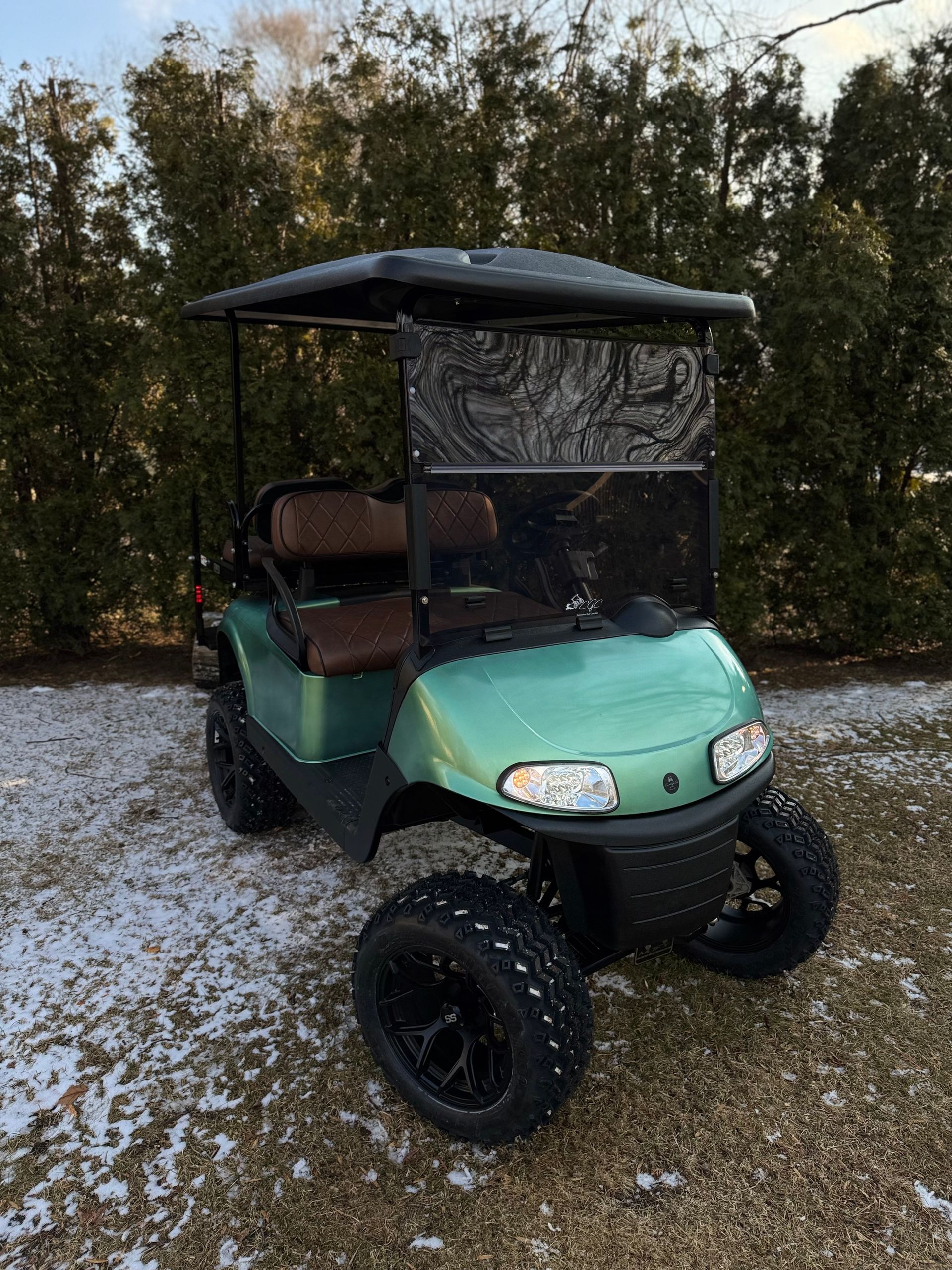 A green golf cart is parked in the snow in a driveway.