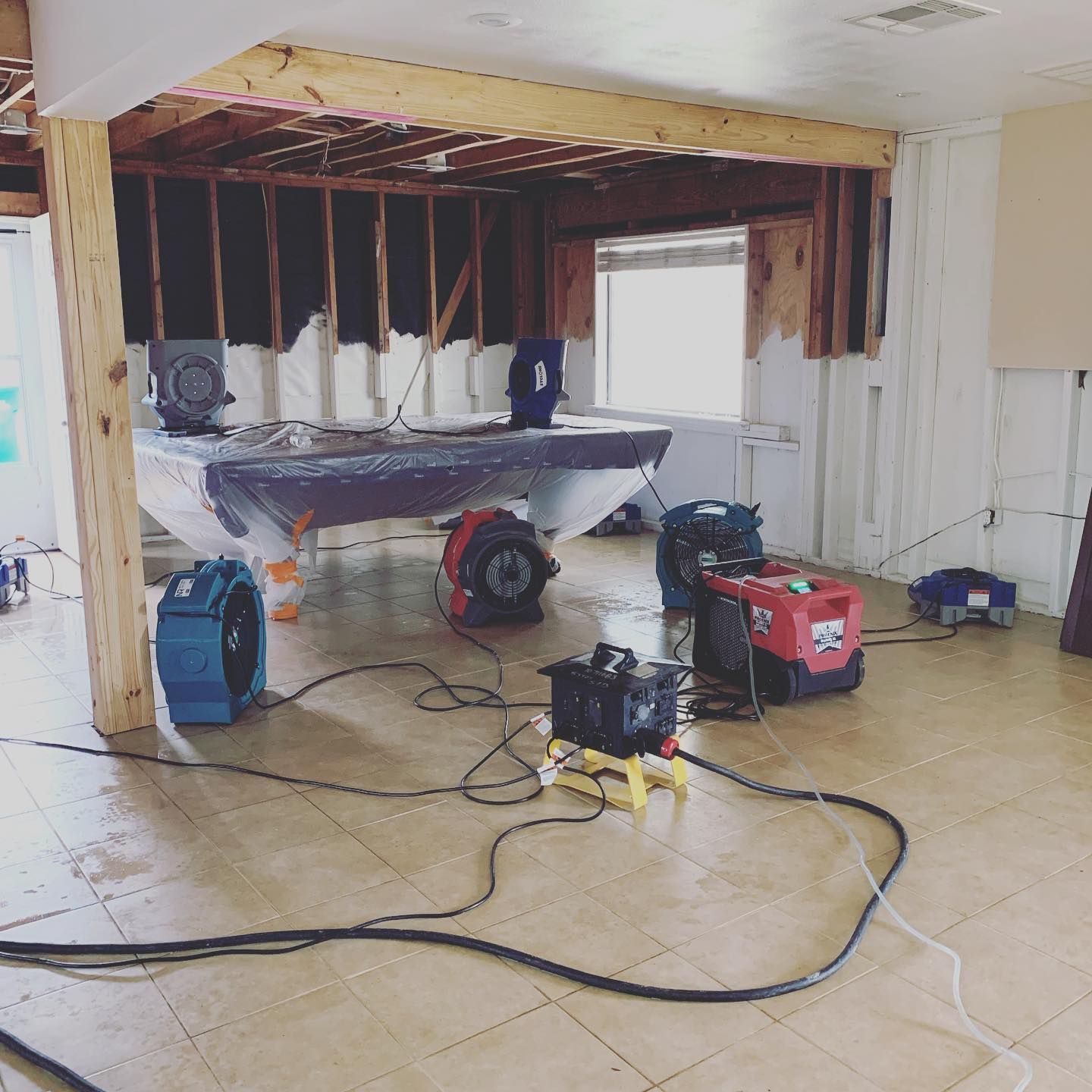 Room in disrepair, flood damage. Drying fans, exposed wall studs, tarps, and wet floor.