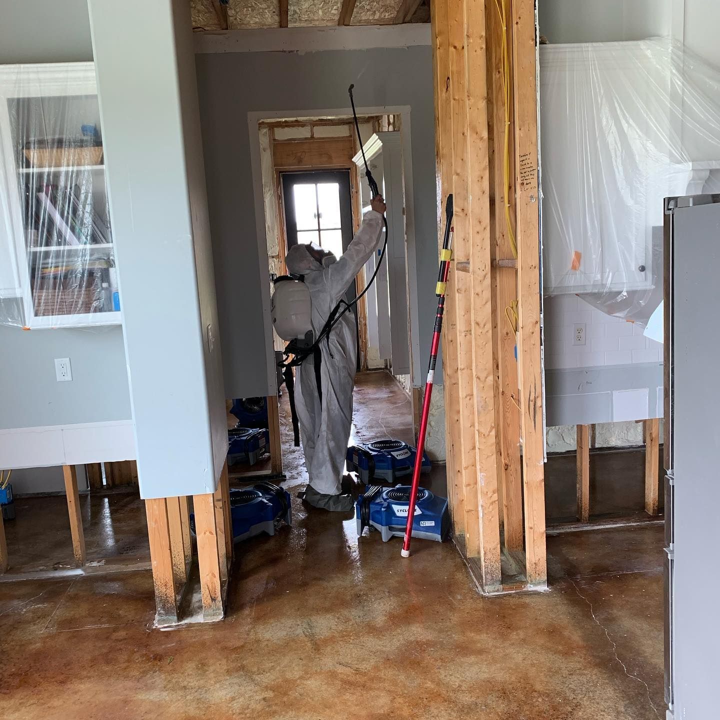 Person in protective suit sprays a water damaged room with standing water.
