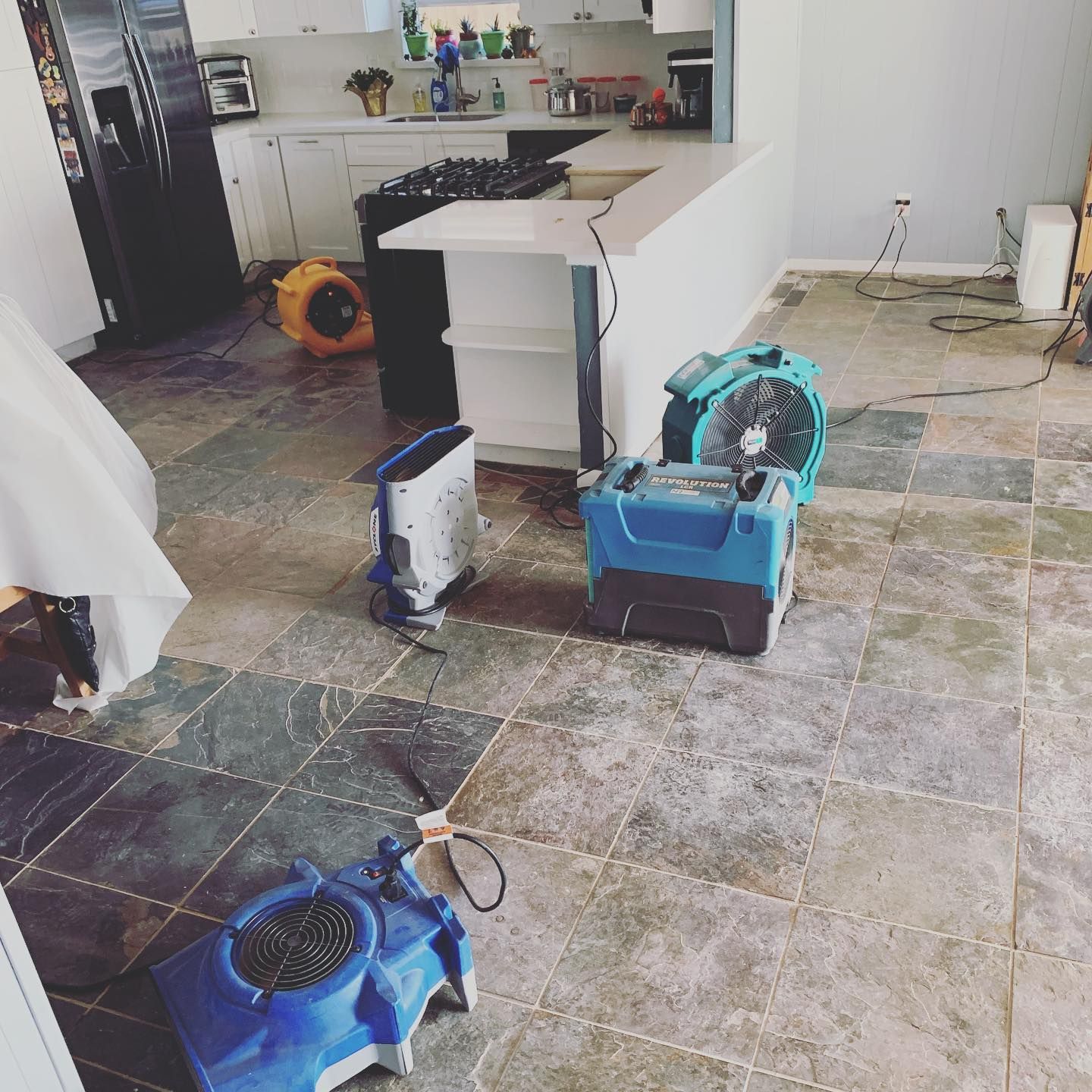 Water damage restoration in a kitchen; fans and equipment drying slate tile floor.