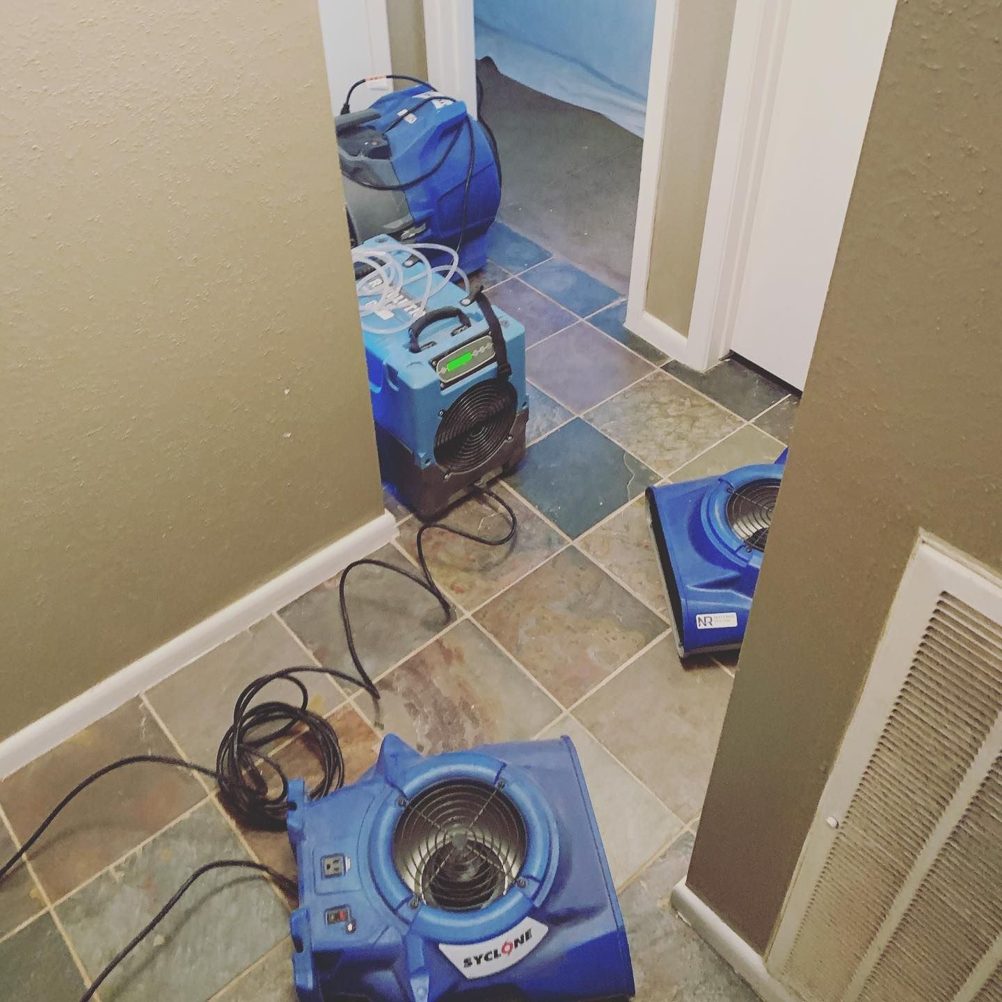 Blue dehumidifiers drying a hallway with tile flooring.