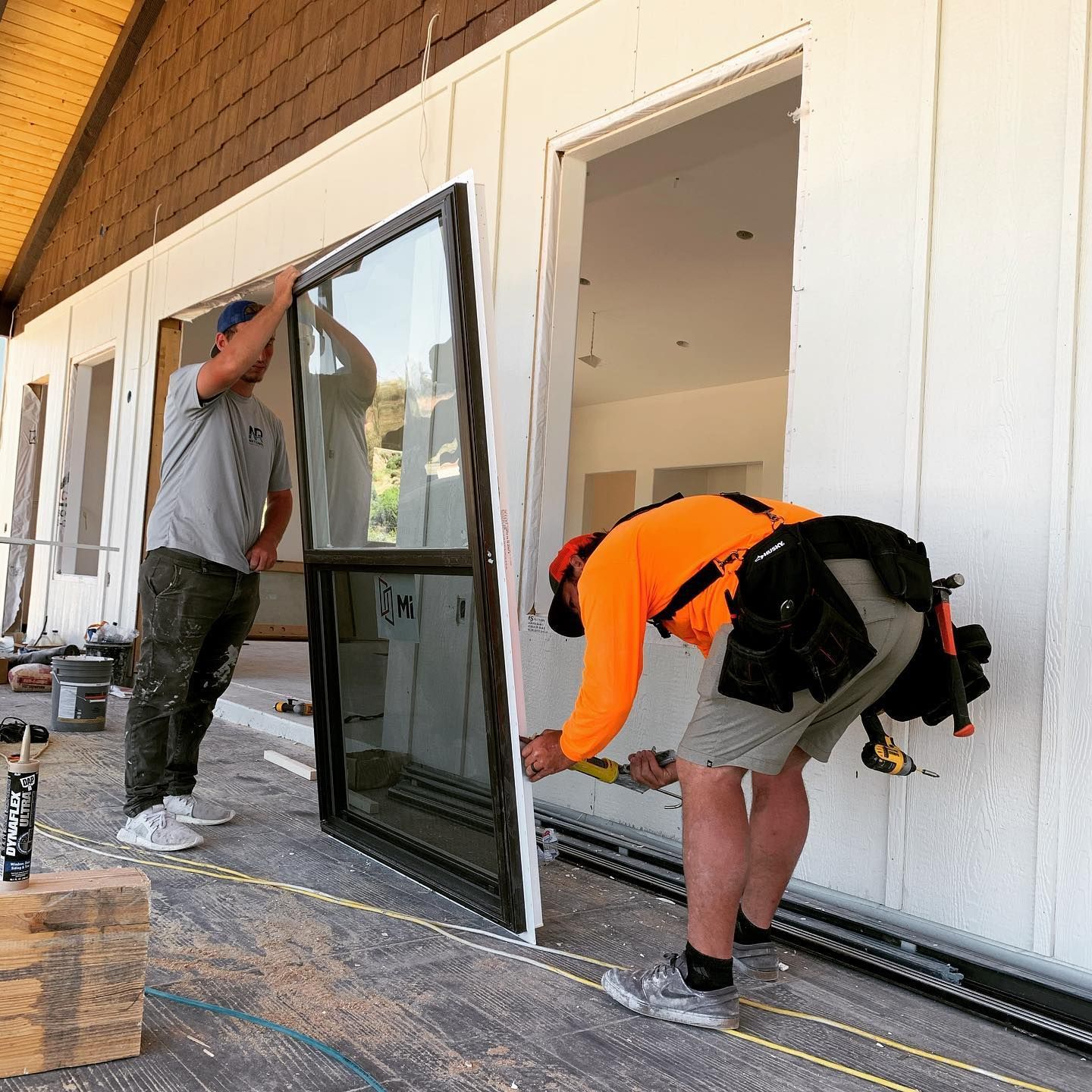 Two construction workers installing a large glass door on a building's exterior.