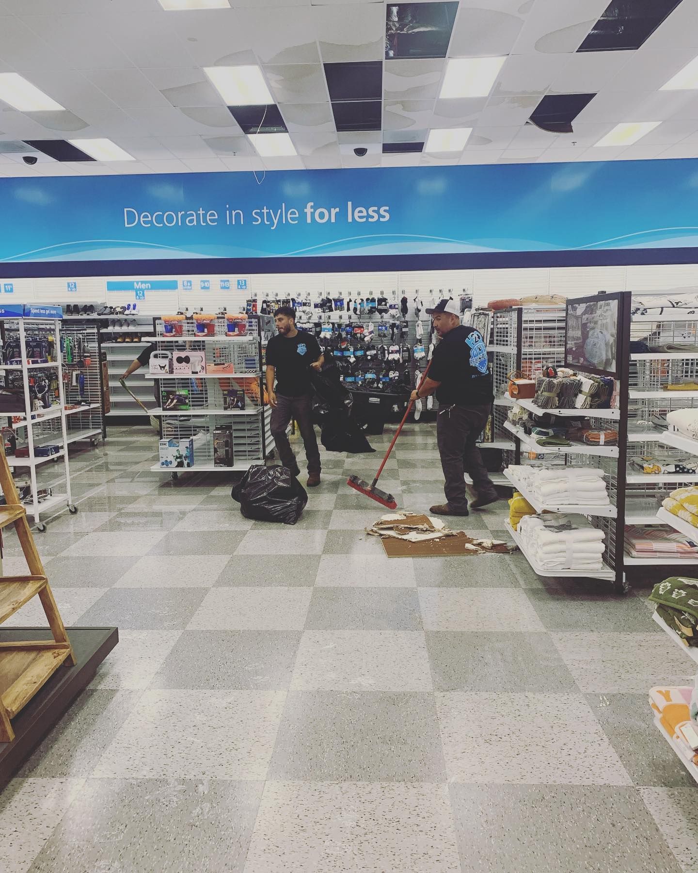 Two men sweeping and bagging items in a Ross store, shelves in the background.