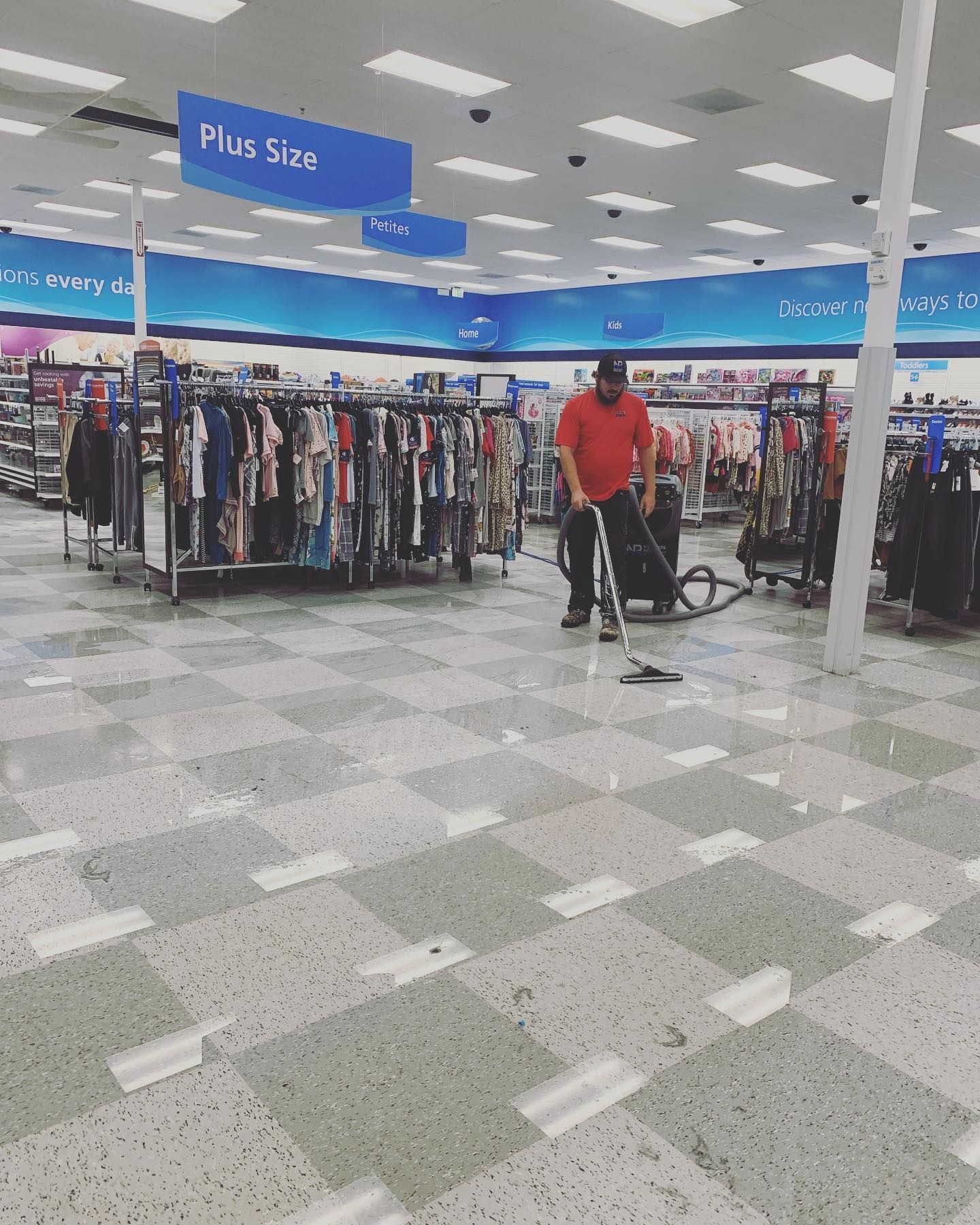 A man vacuums the floor in a clothing store, beneath blue 