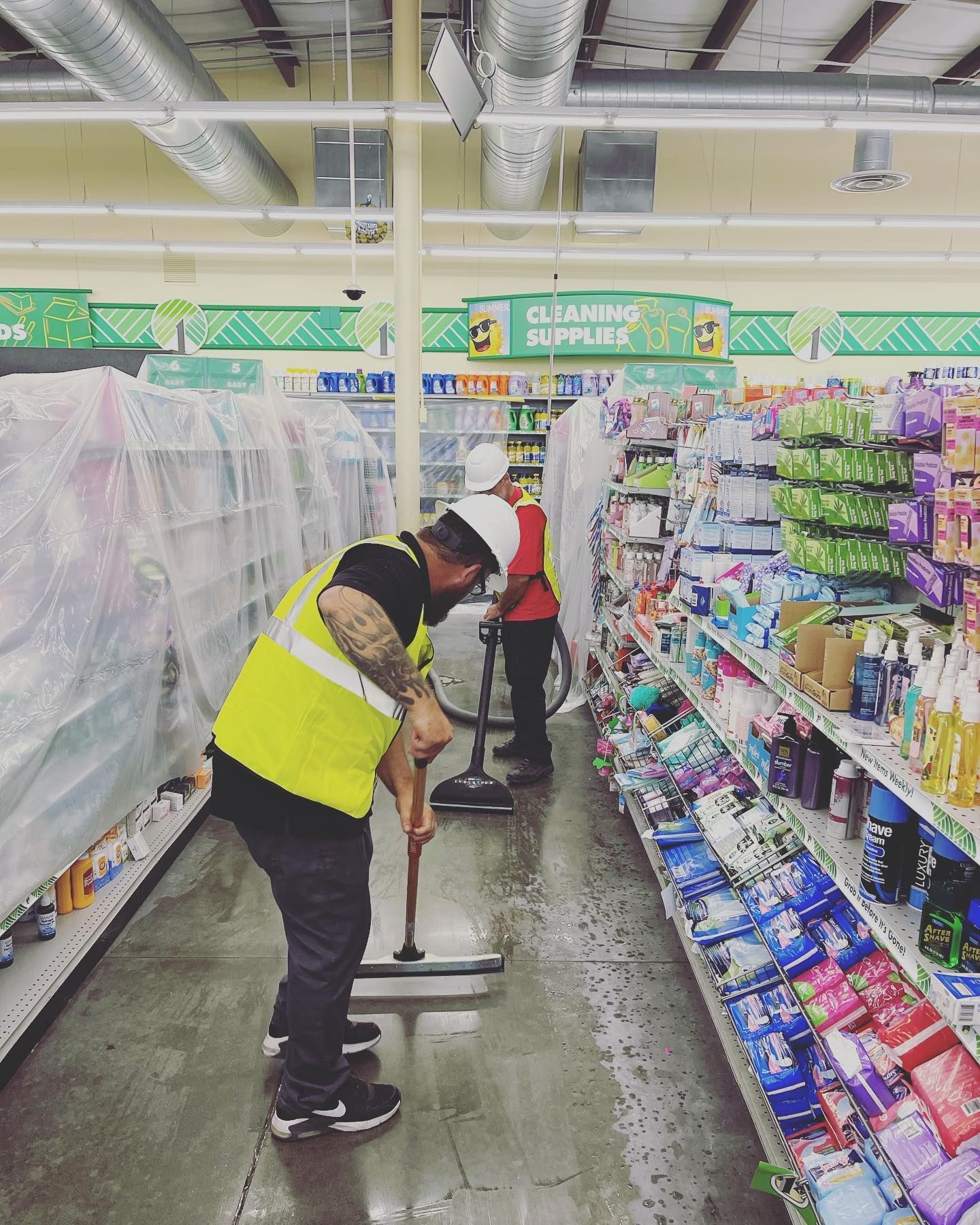 Workers mopping a Dollar Store floor. Shelves are covered in plastic, fluorescent lights overhead.