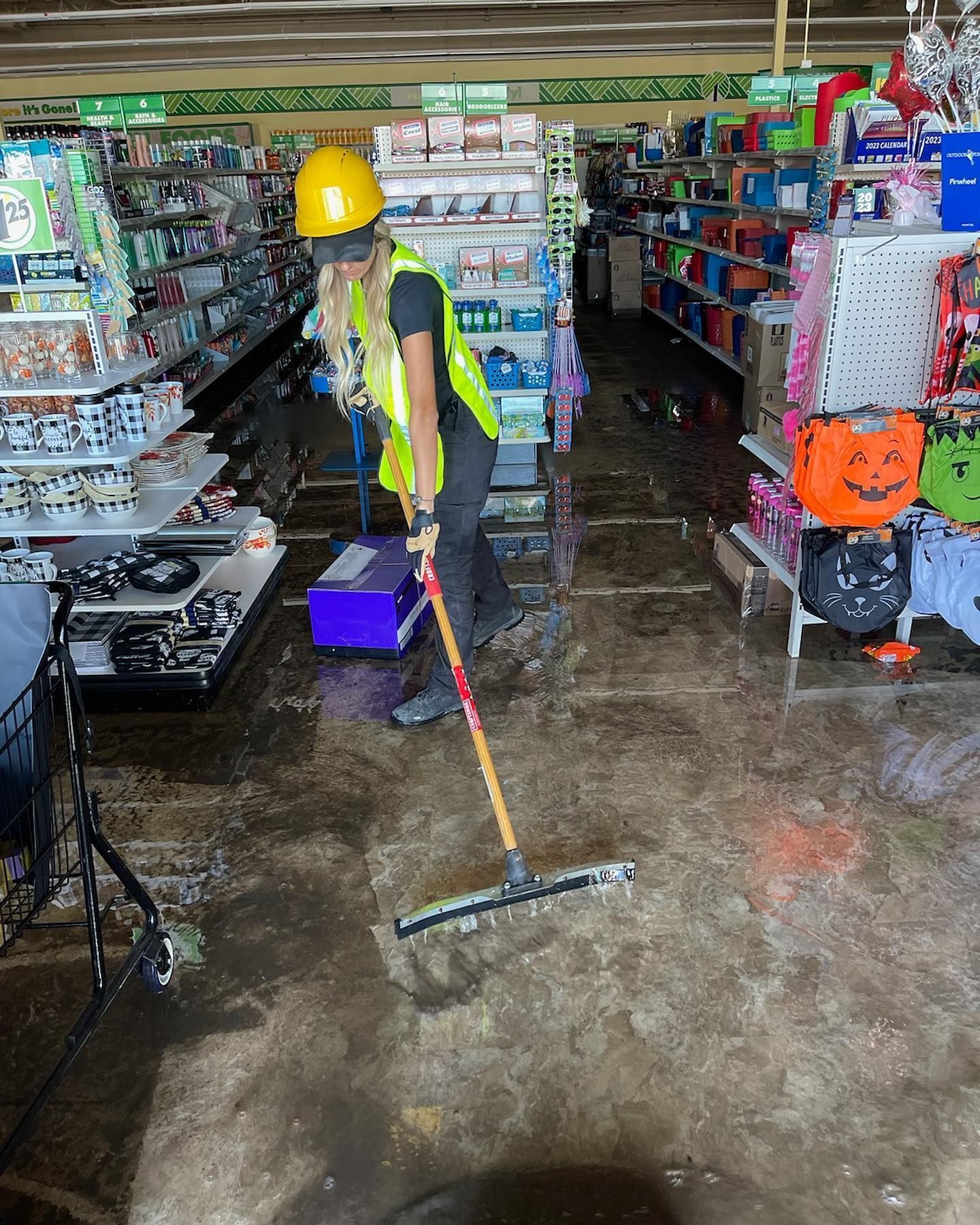 Woman in safety gear mopping a flooded Dollar store.