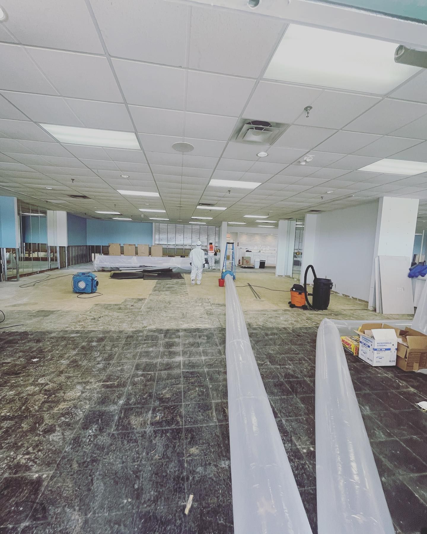 Interior of a commercial space under renovation, workers in protective suits, exposed floor, debris.