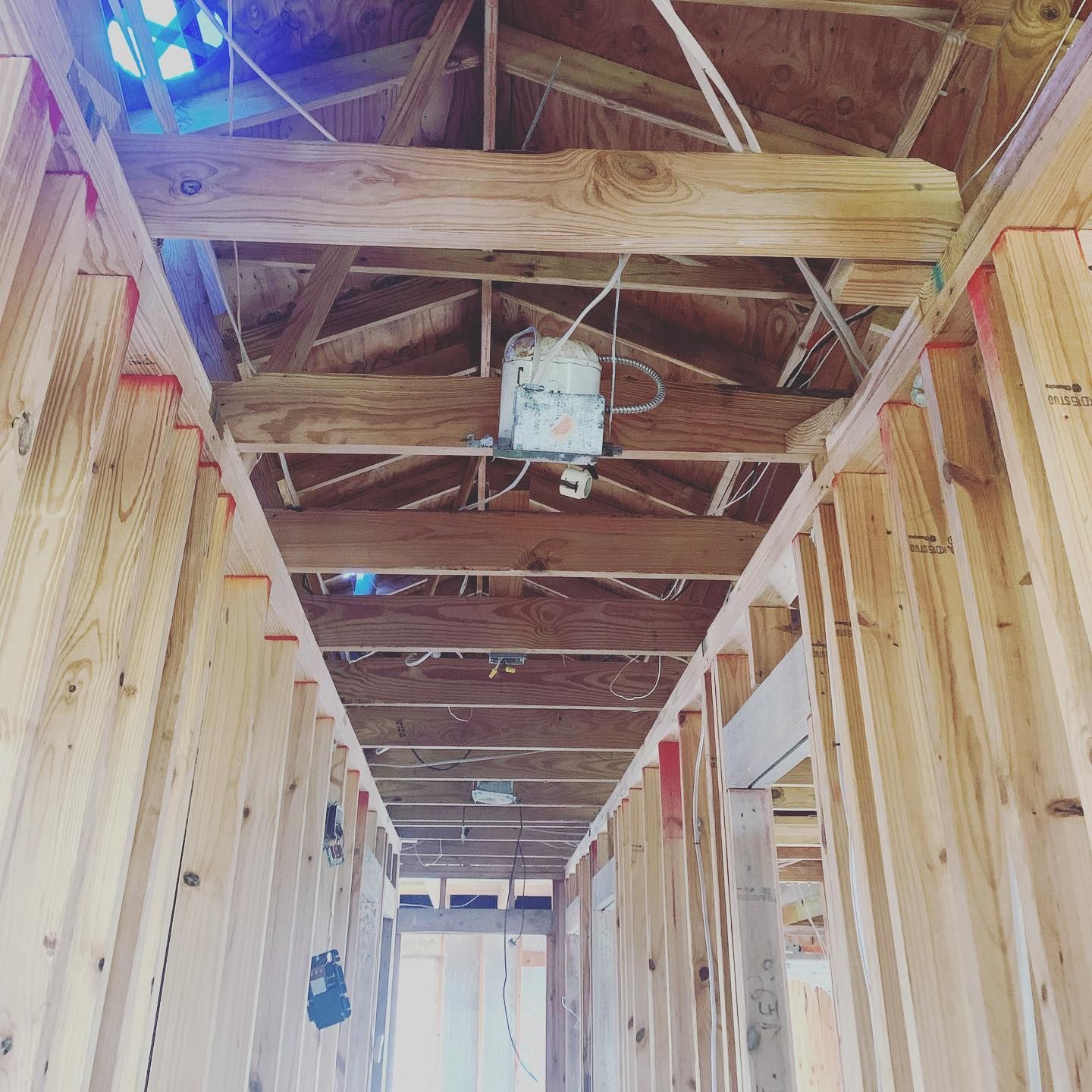 Interior of a building under construction, showcasing exposed wooden beams and framework, with overhead lighting.