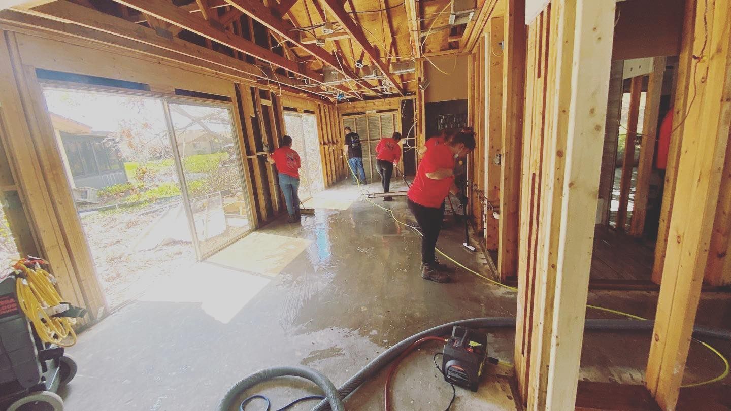 People in red shirts working on a building's interior. Exposed framing, concrete floor, and sliding glass doors.