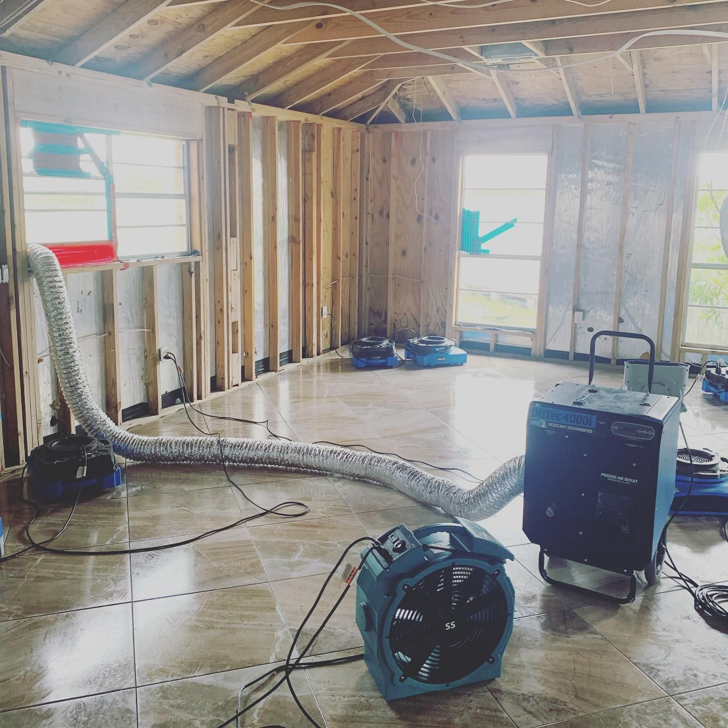 Interior room with drying equipment after a flood. Fan, dehumidifier, and ductwork on tiled floor.