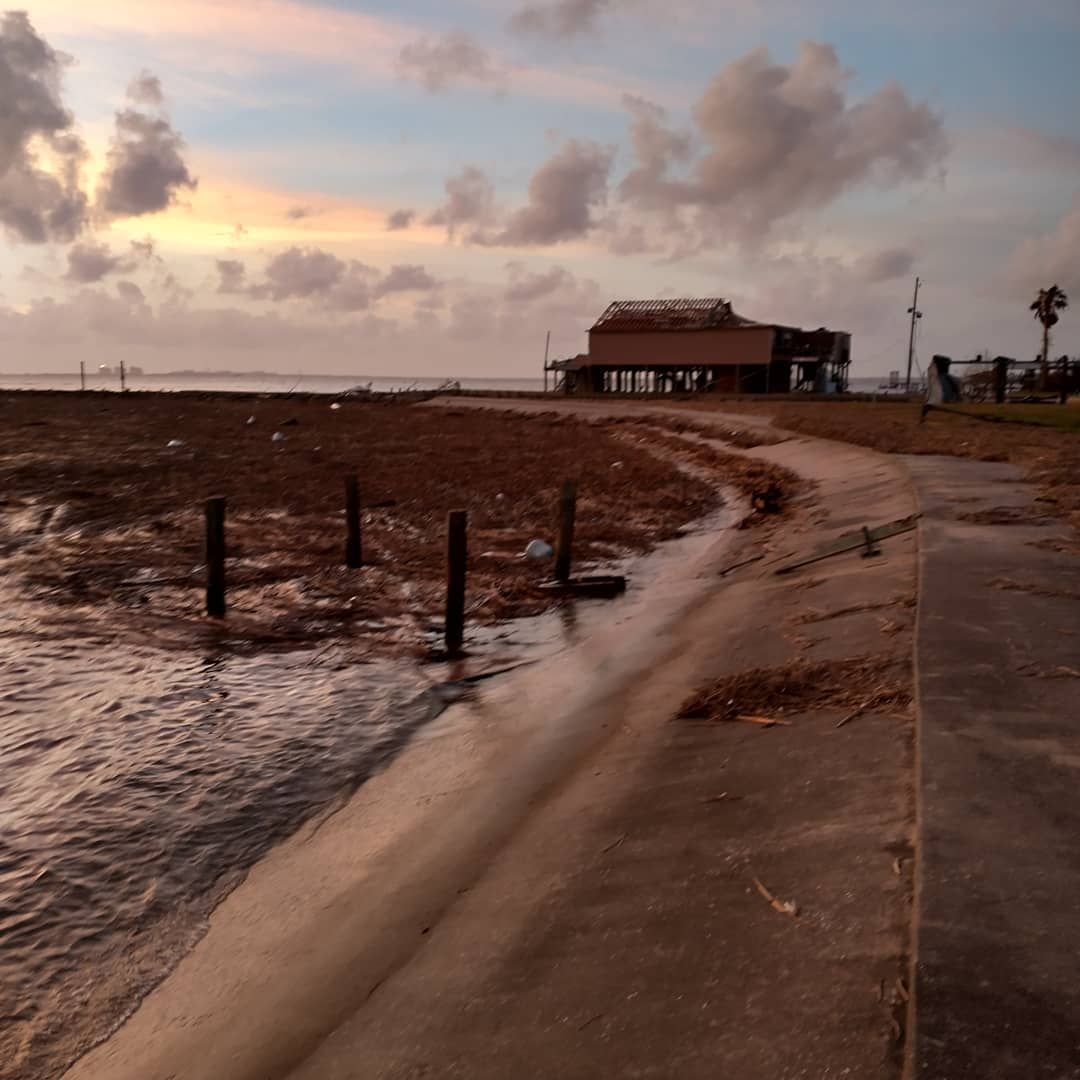Coastal scene at dusk; water, pier, debris on shore, and cloudy sky.