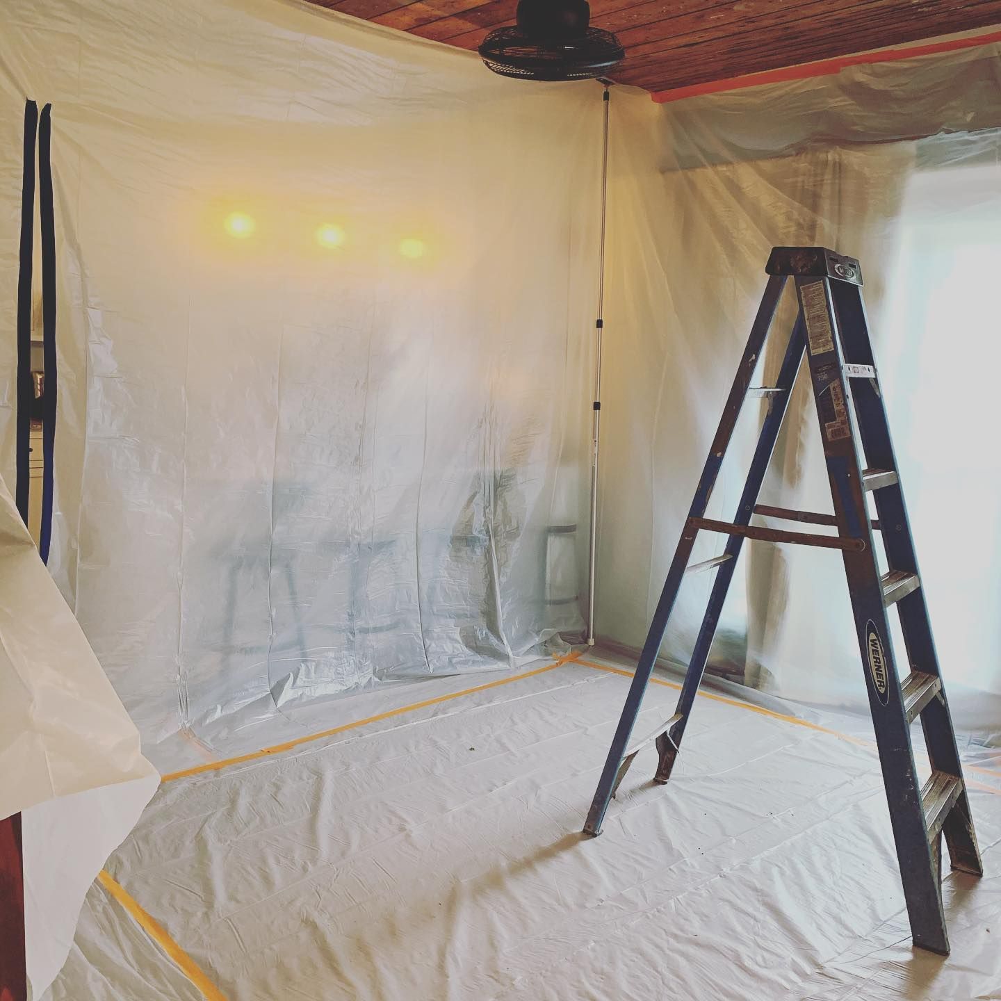 Room covered in plastic sheeting, ladder, and string lights.
