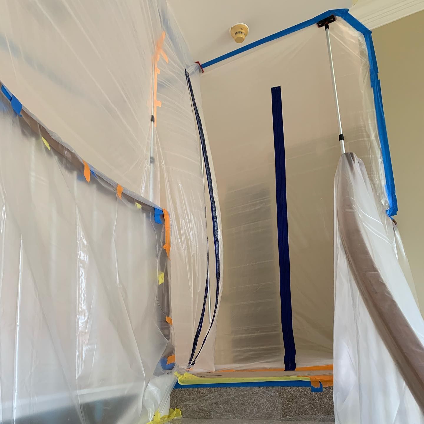 Staircase covered with plastic sheeting, blue and orange tape, for construction or remediation.