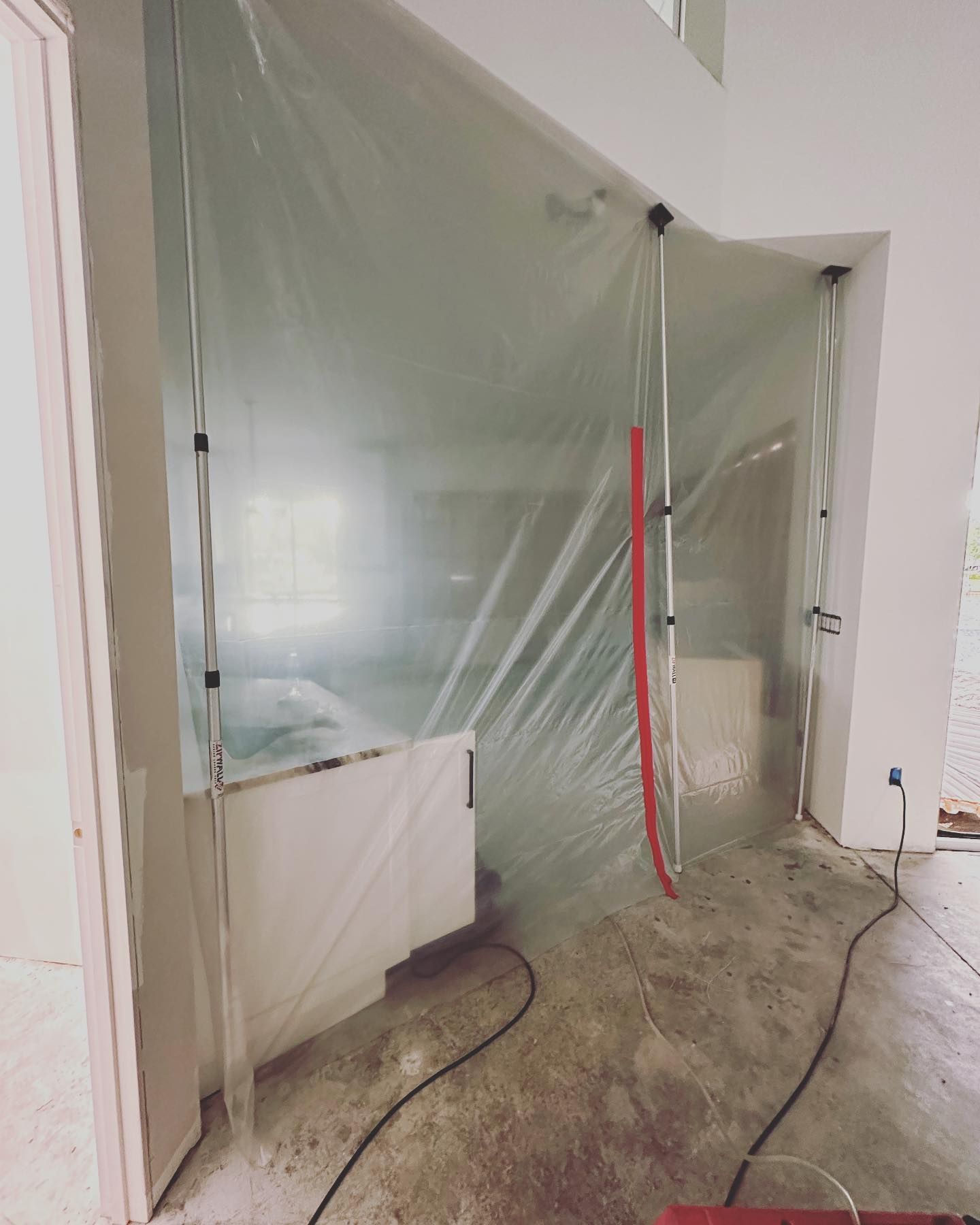 Plastic sheeting encloses a room under construction, likely for dust control. Black cables run across a concrete floor.