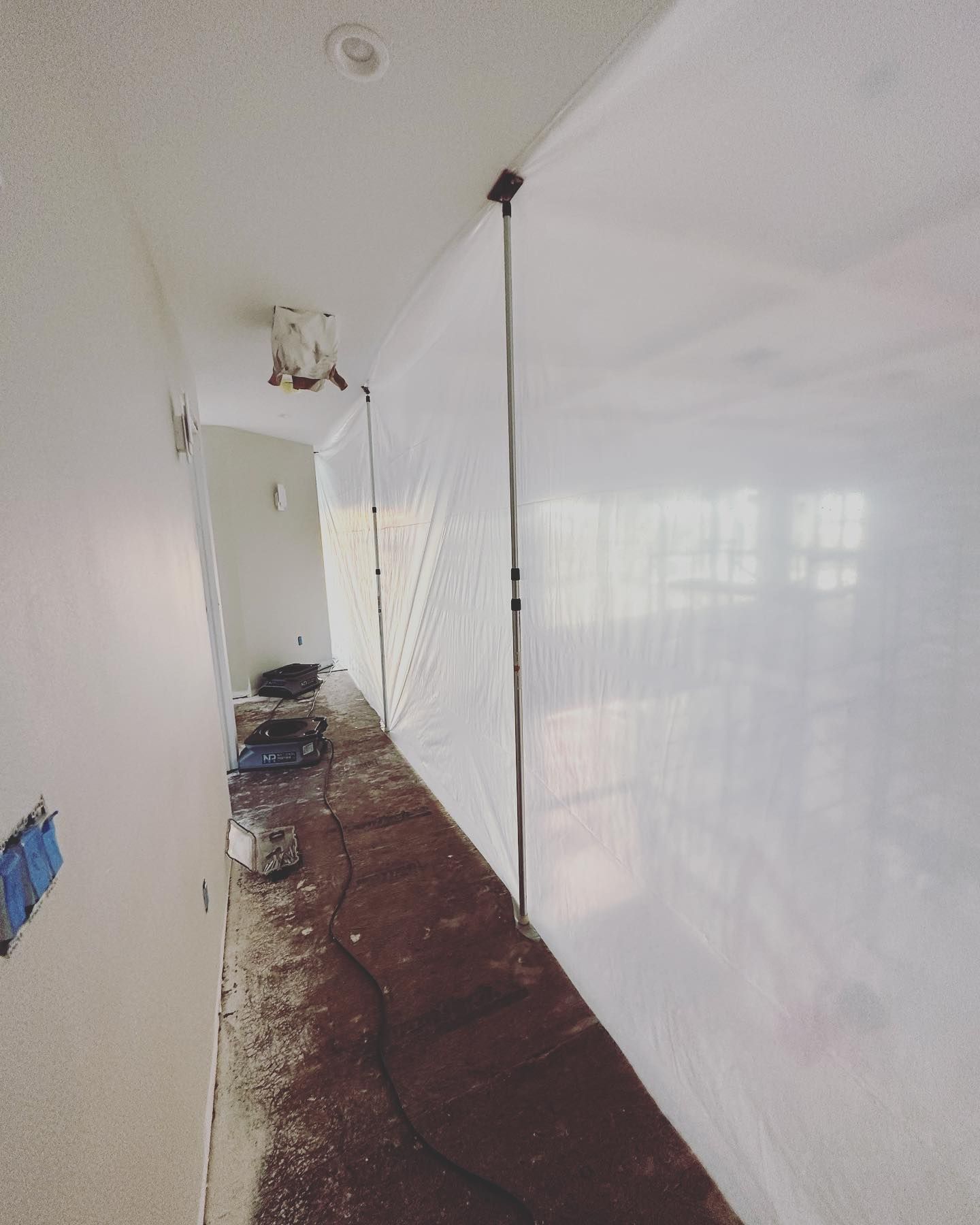 Hallway with plastic sheeting, dust, and electrical outlets, likely under construction.