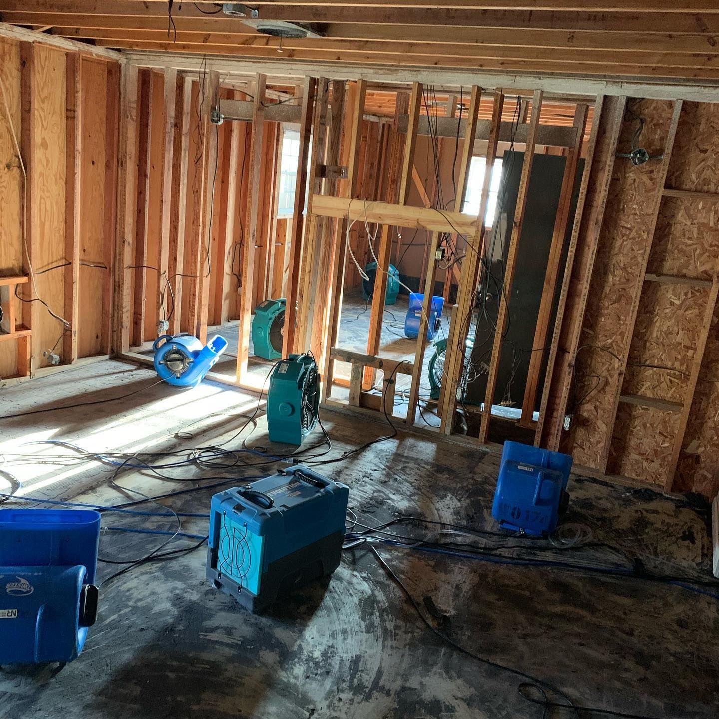 Interior of a building under construction, showing exposed wooden framing and multiple blue dehumidifiers.