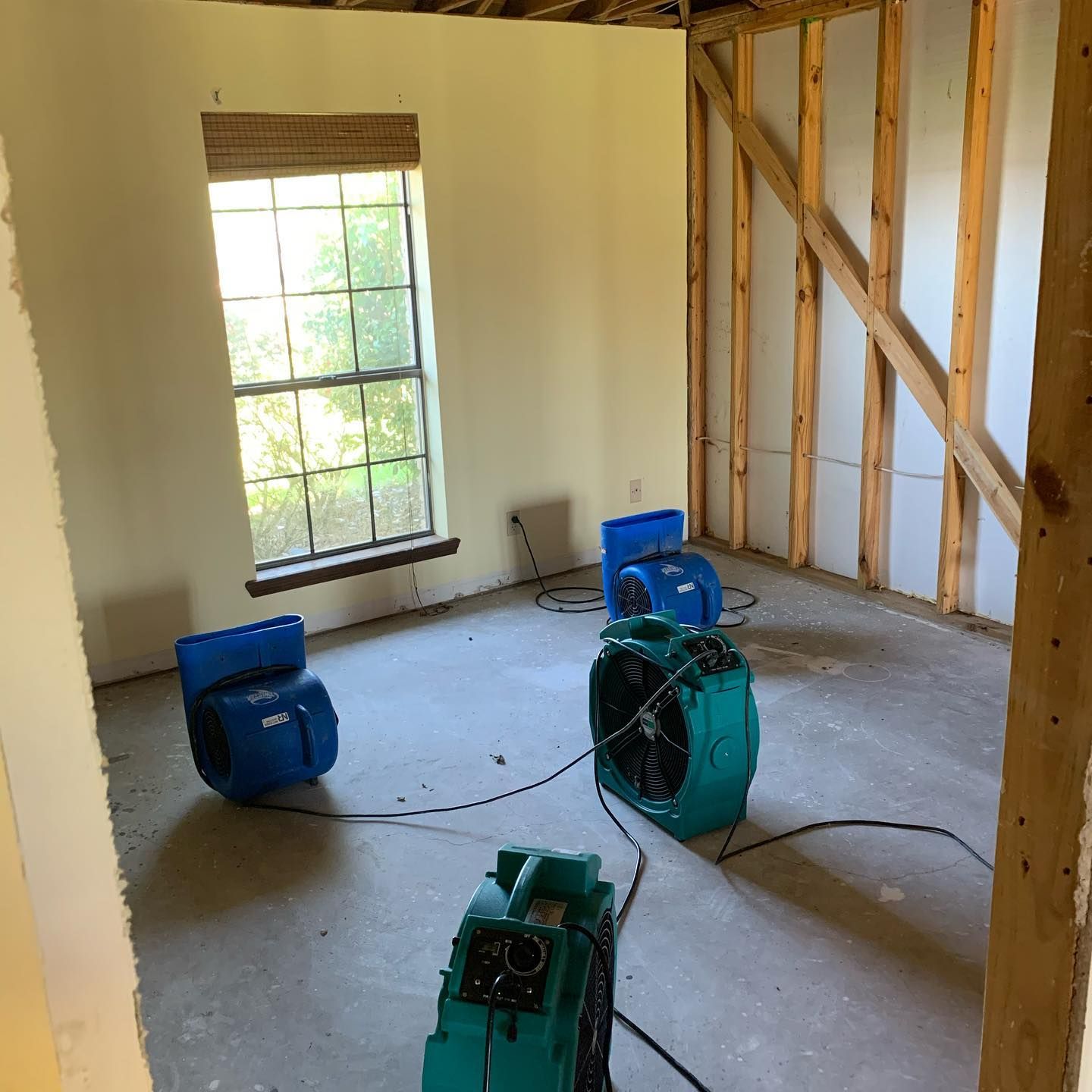A room with fans drying it out after possible water damage. Window on the left, open studs on the right.