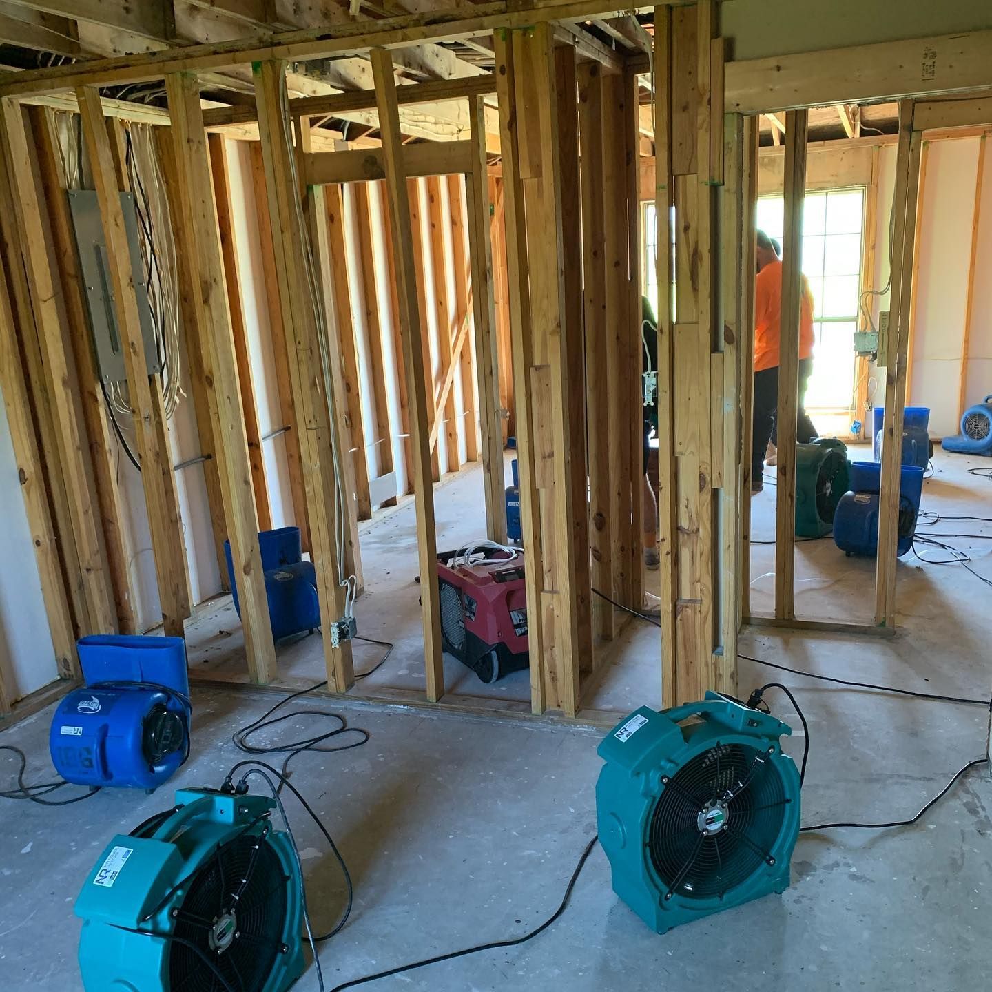 Interior view of a room under renovation with drying equipment and a worker visible.