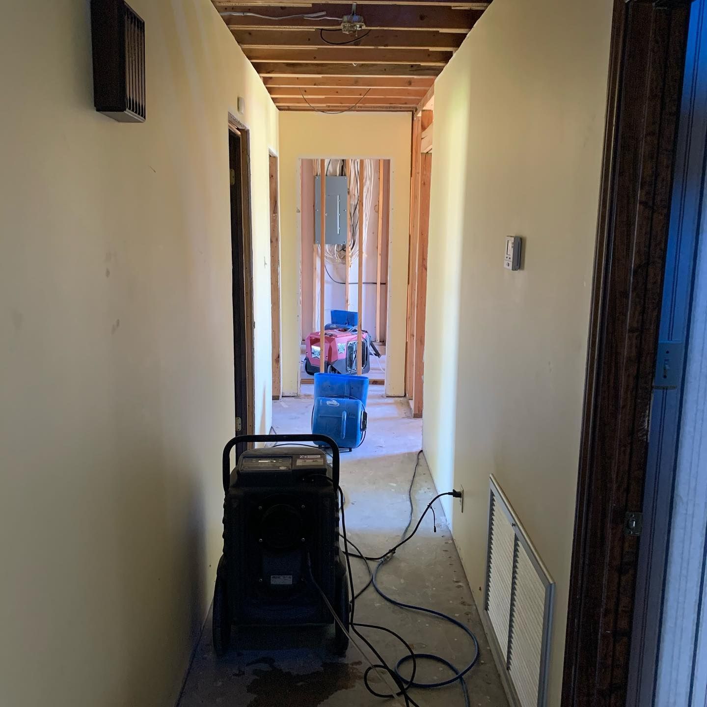 Hallway under renovation with exposed ceiling beams and dehumidifier.