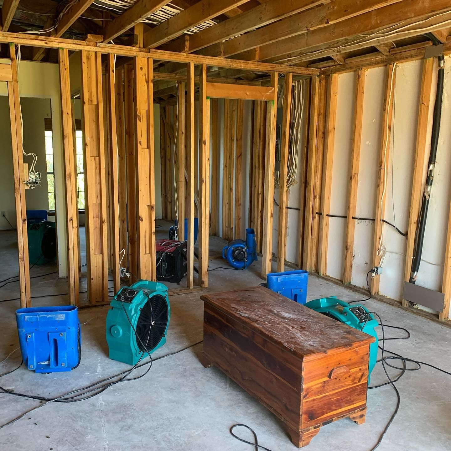 Room with exposed wooden framing and fans drying out interior.