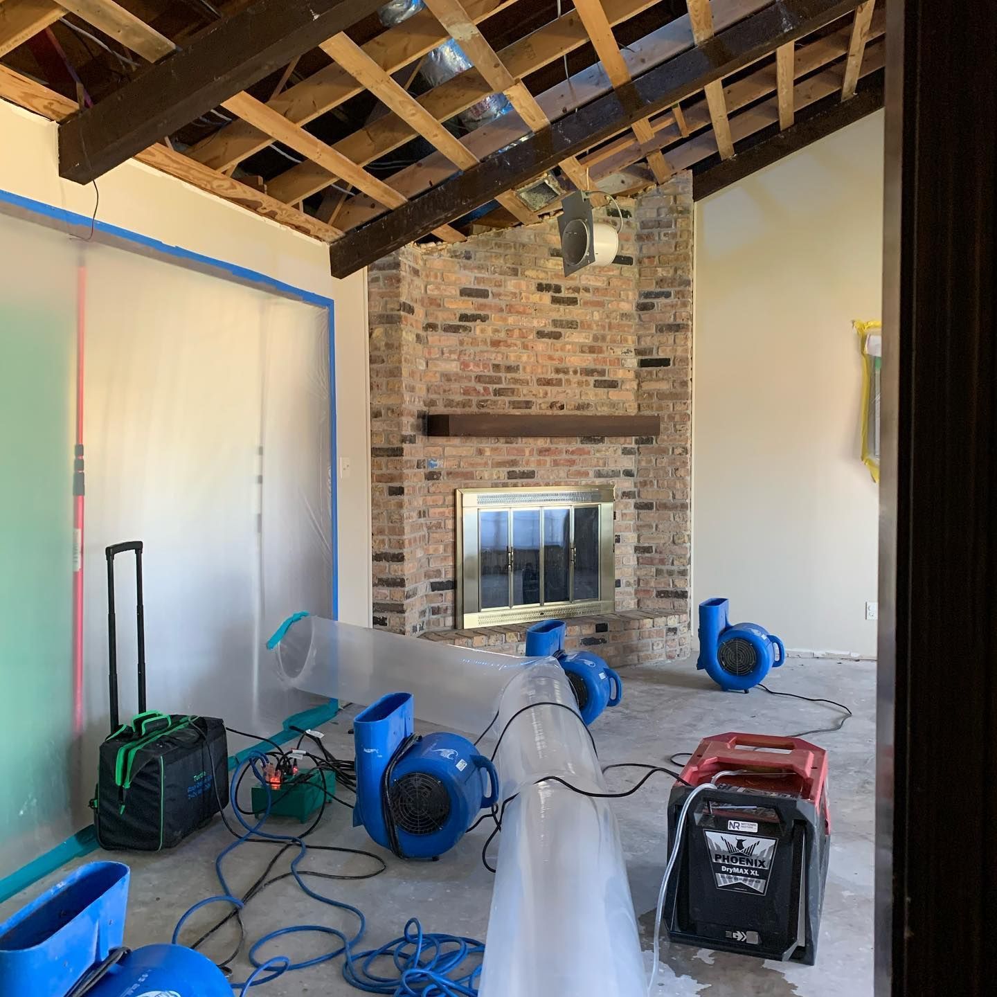 A room undergoing water damage restoration with fans, plastic sheeting, and a brick fireplace.
