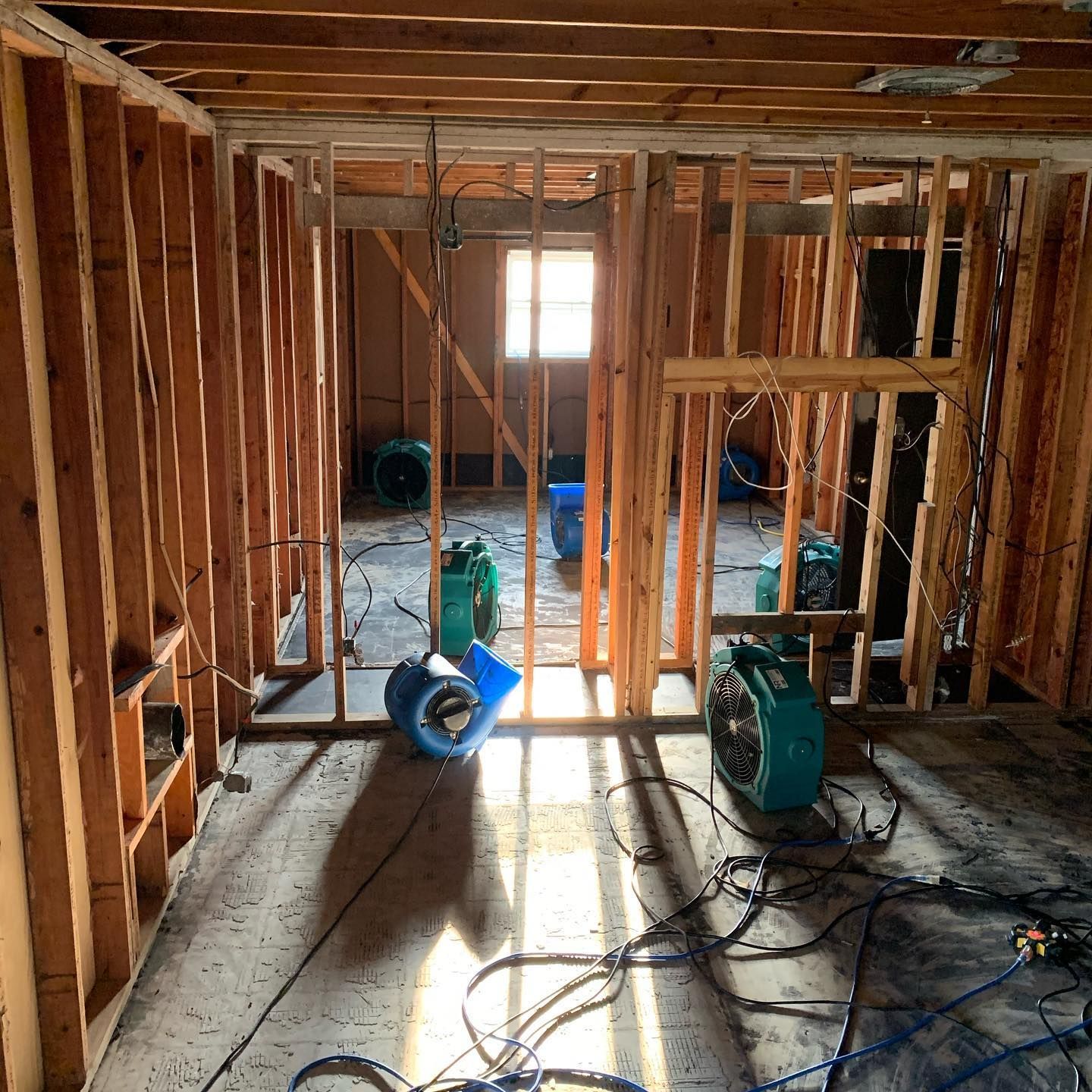 Interior framing of a room under construction with ventilation fans and exposed wiring on the floor.