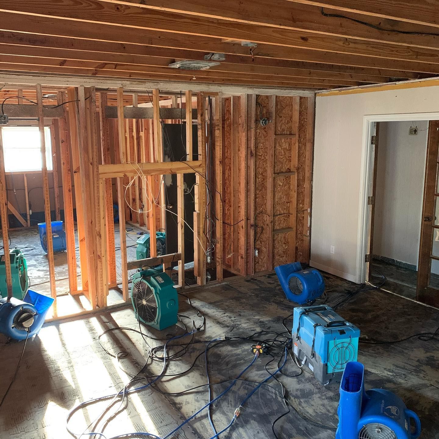 Interior view of a room undergoing flood damage restoration with several air movers running on the concrete floor.