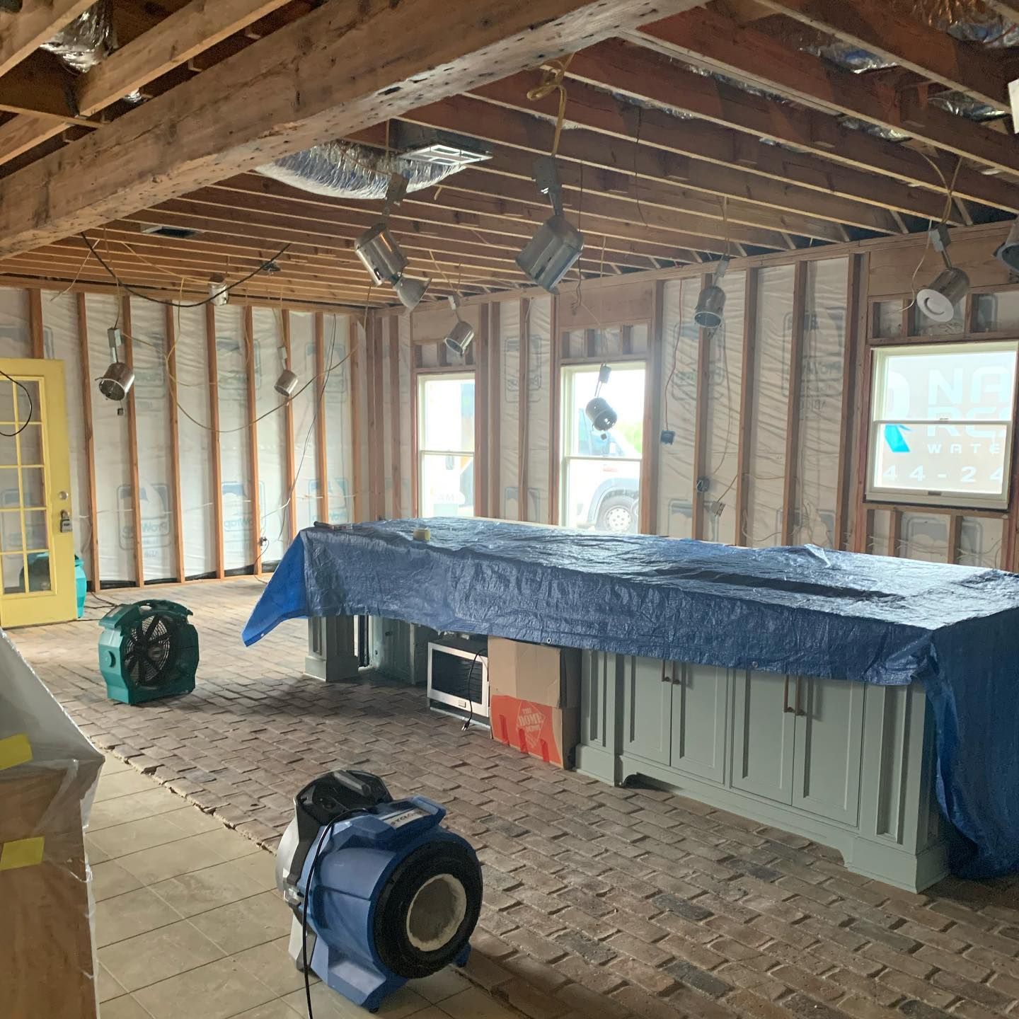 Interior room under construction with exposed beams and walls, a covered island, and drying equipment.