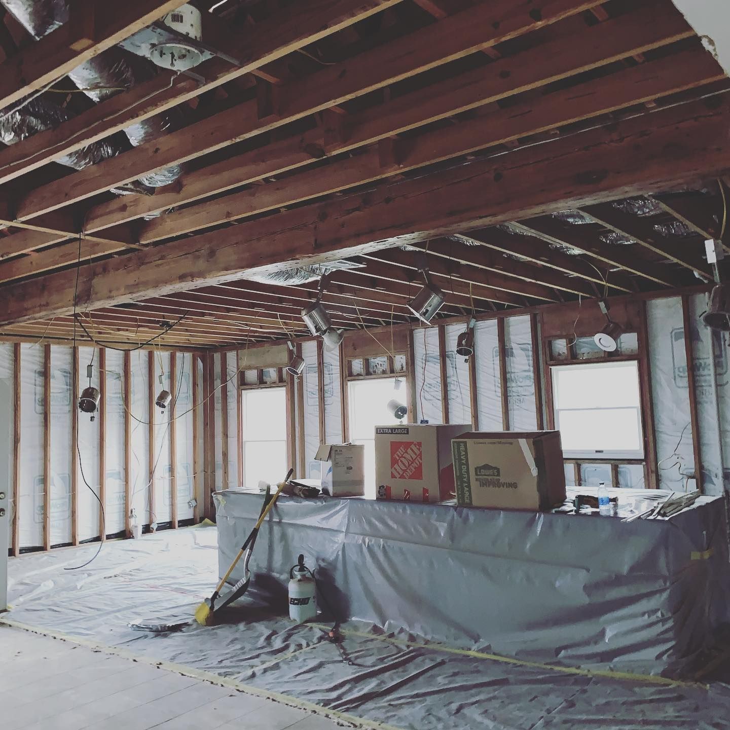Interior of a house under construction, with exposed beams and insulation, visible windows and boxes.