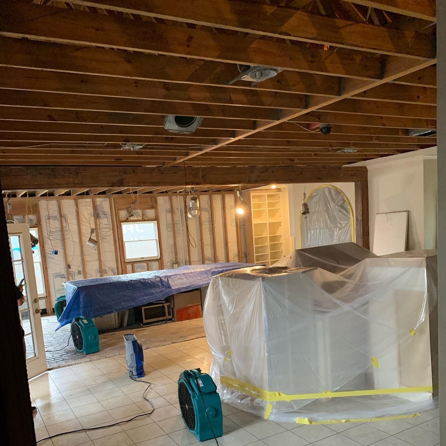 Renovation work: Interior view with exposed ceiling beams, fans, and covered furniture.