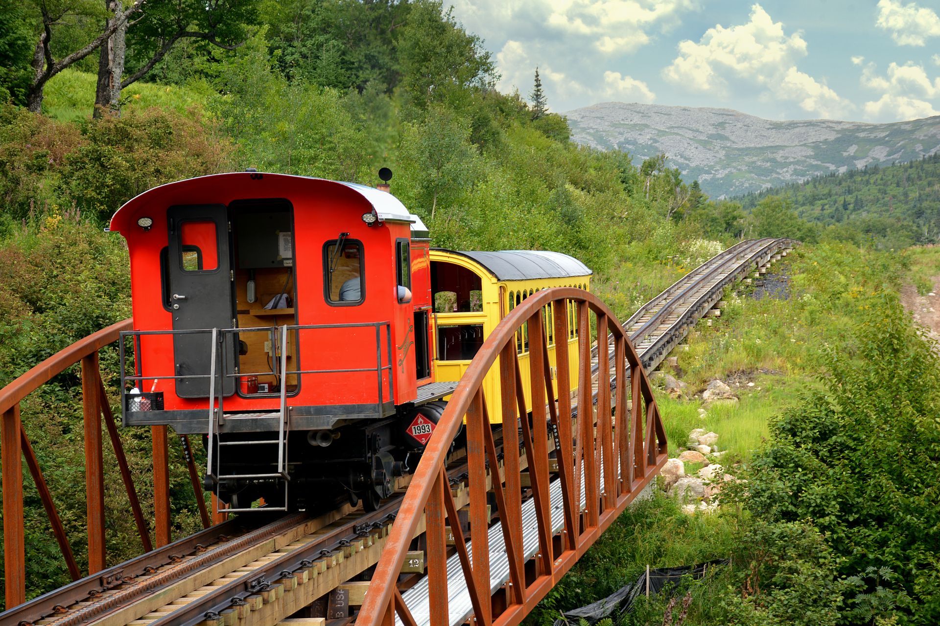 A red and yellow train is going over a bridge.