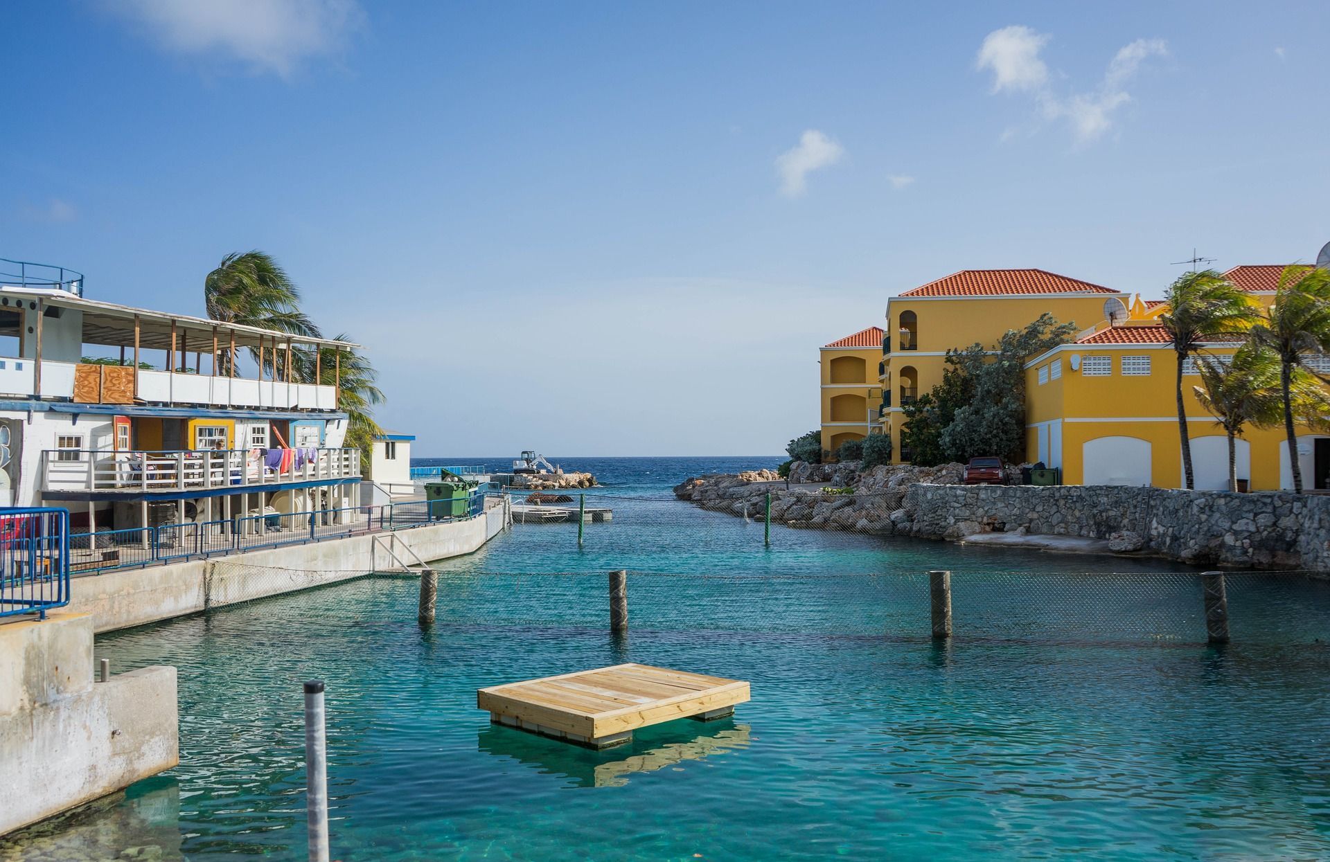 A dock in the middle of a body of water with a yellow building in the background.