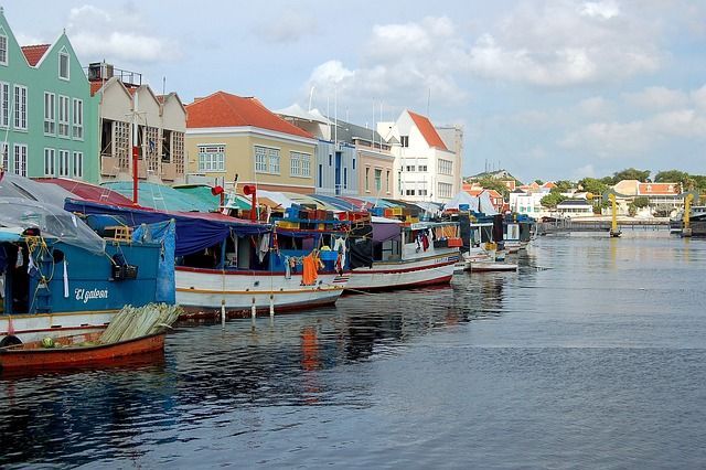 A row of boats are docked in a harbor with buildings in the background