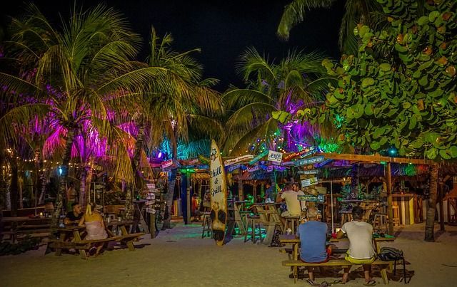 A group of people are sitting at picnic tables on a beach at night.