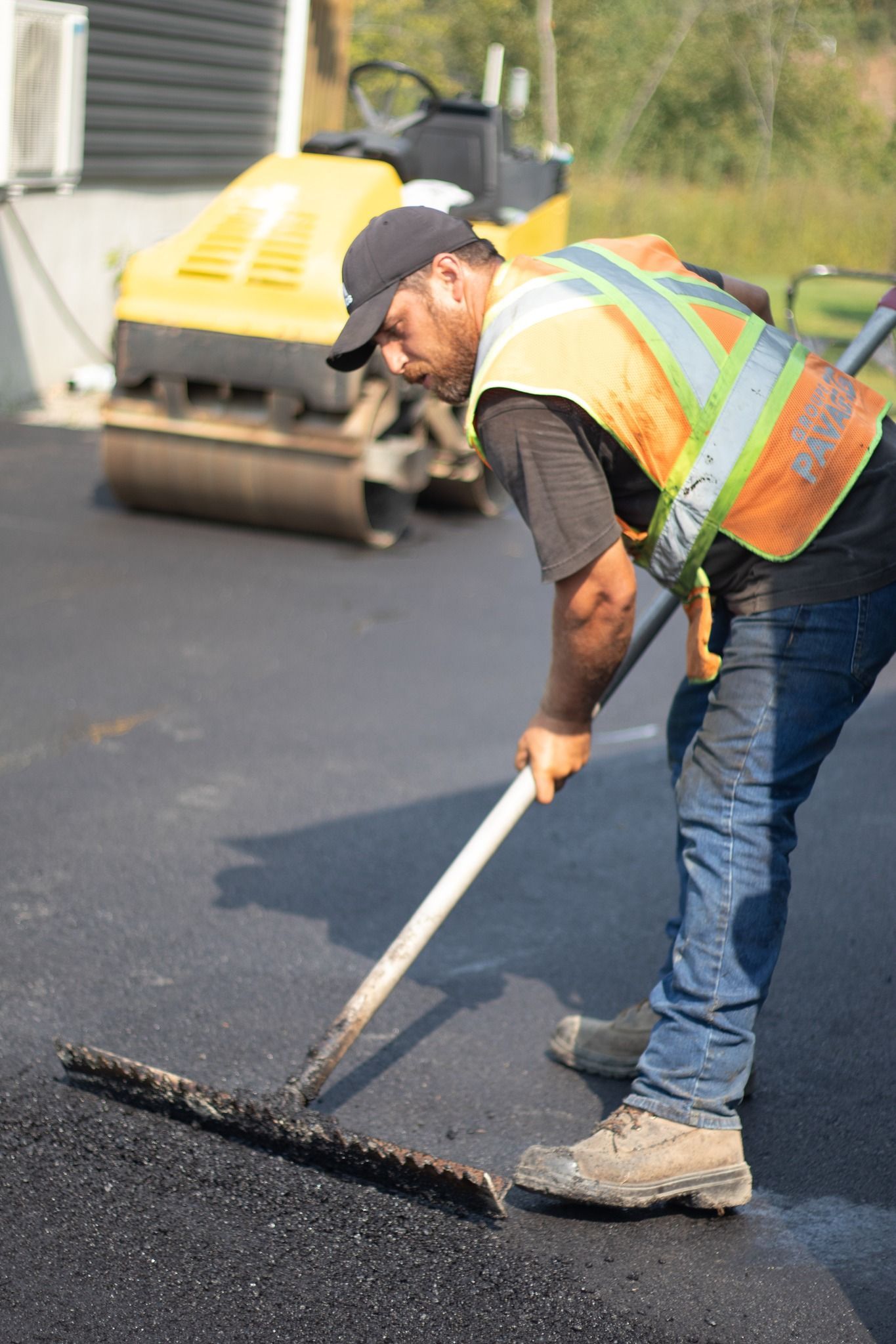 Un homme répand de l'asphalte sur une route avec un râteau.