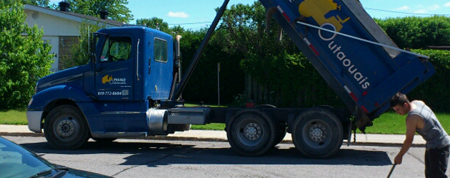 Un homme balaie la rue devant un camion à benne basculante.