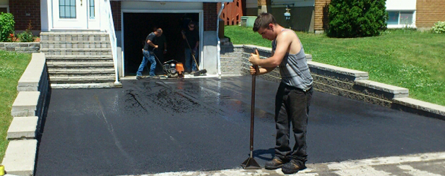 Un homme utilise un balai pour étendre de l'asphalte sur une allée.