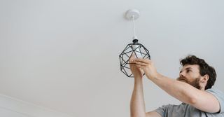 A man is installing a light fixture on the ceiling.